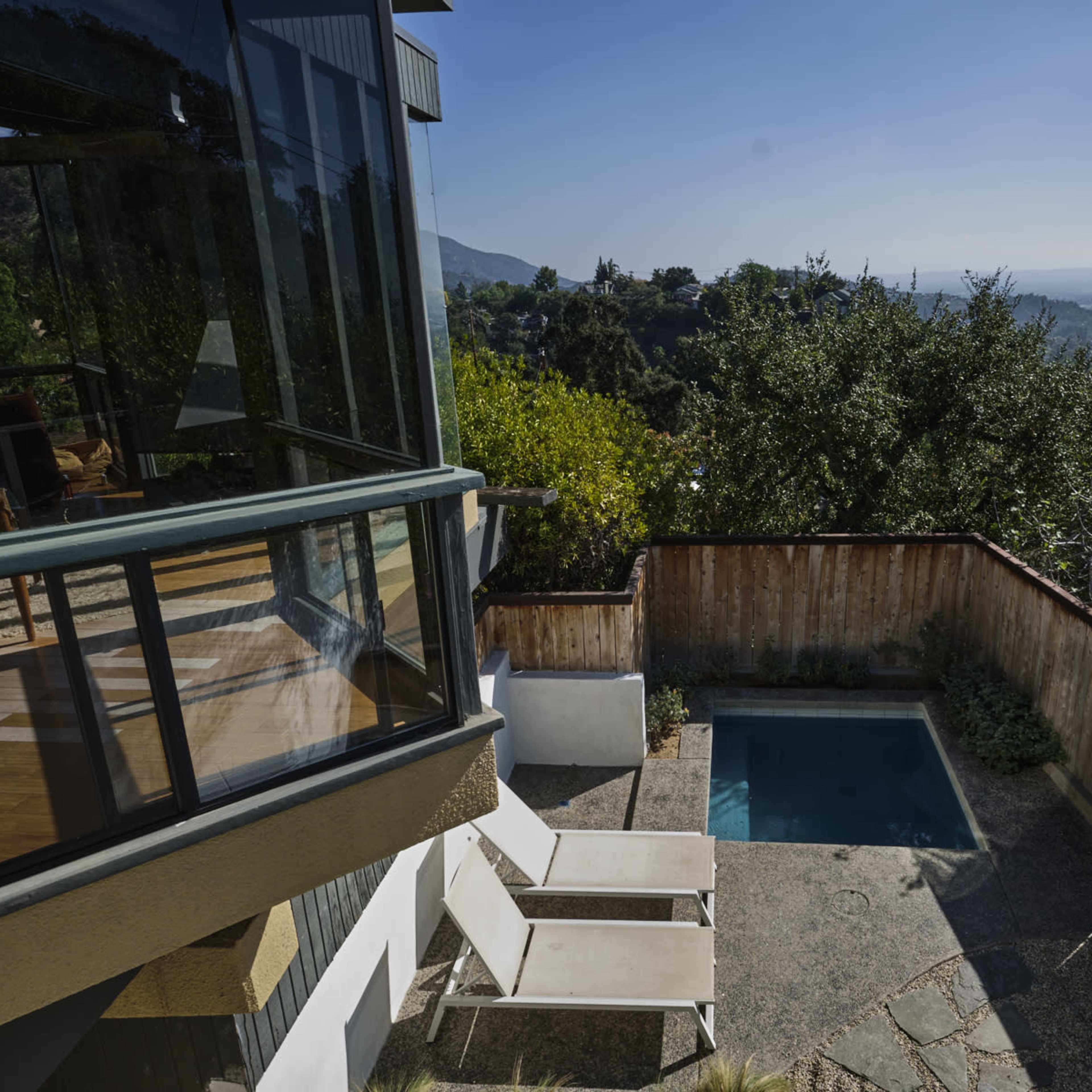 A modern house with large windows overlooks a small pool and a valley filled with trees and distant mountains.
