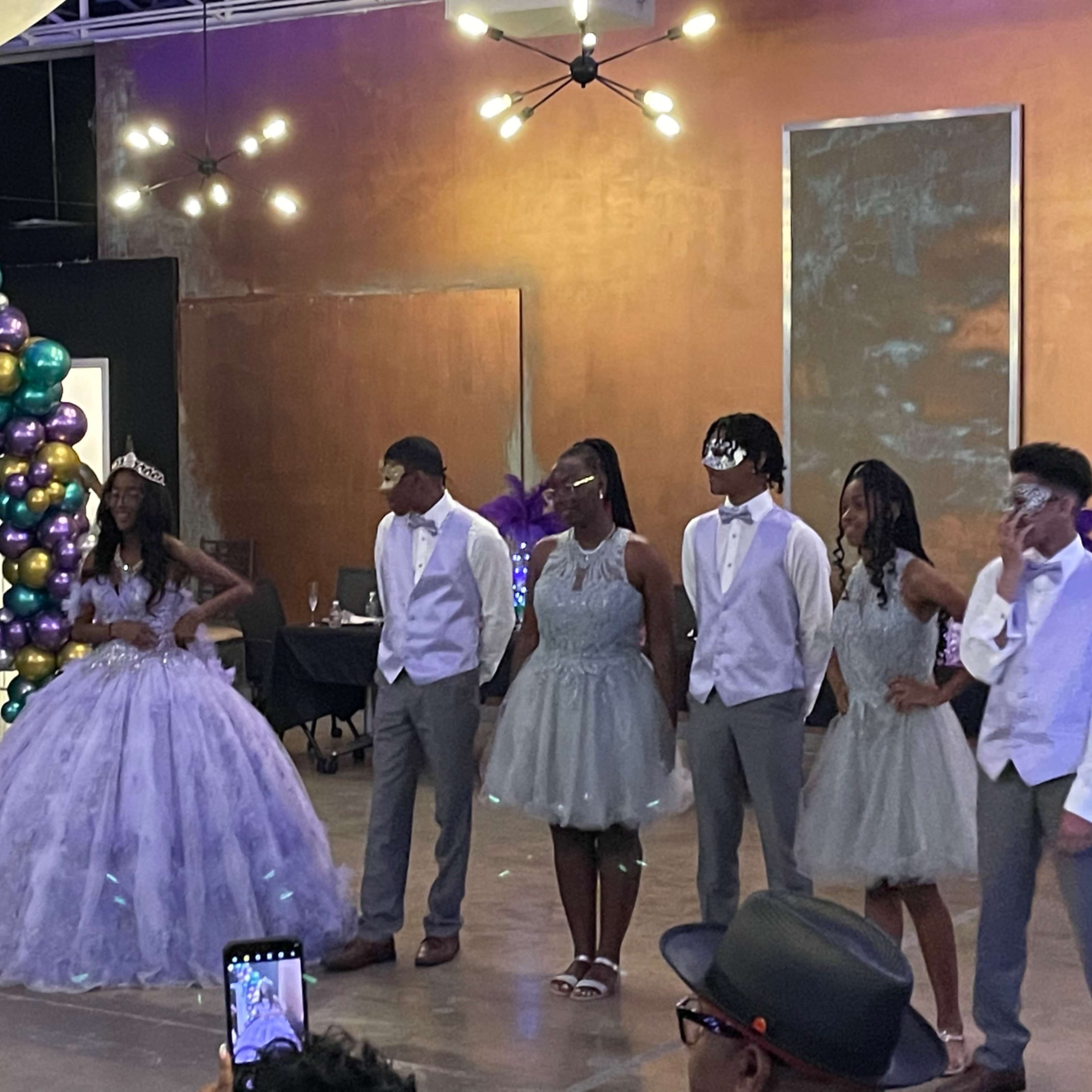 A group of young people stands together in formal attire at a decorated indoor event space.