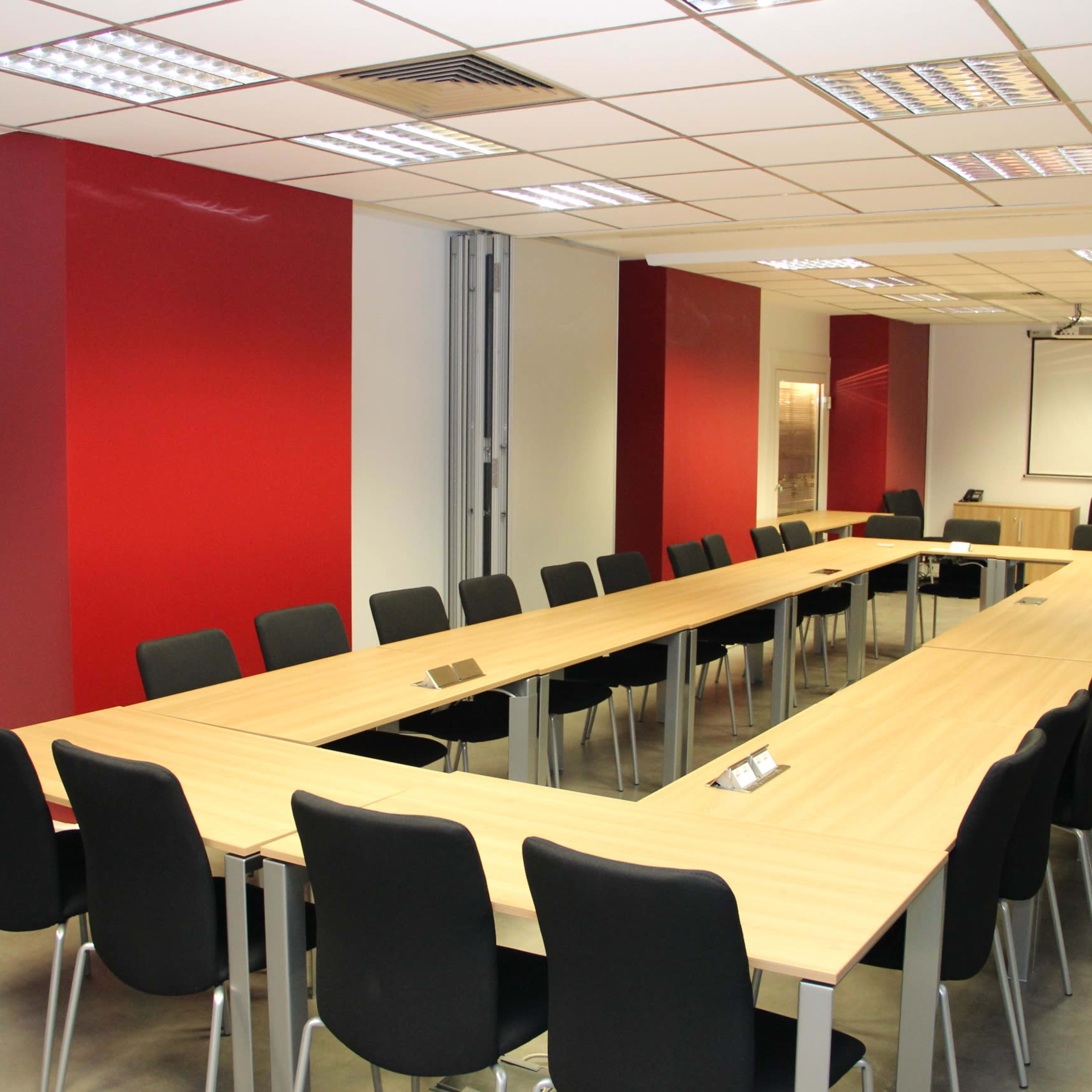 A modern conference room with a long, rectangular table surrounded by black chairs and red accent walls.