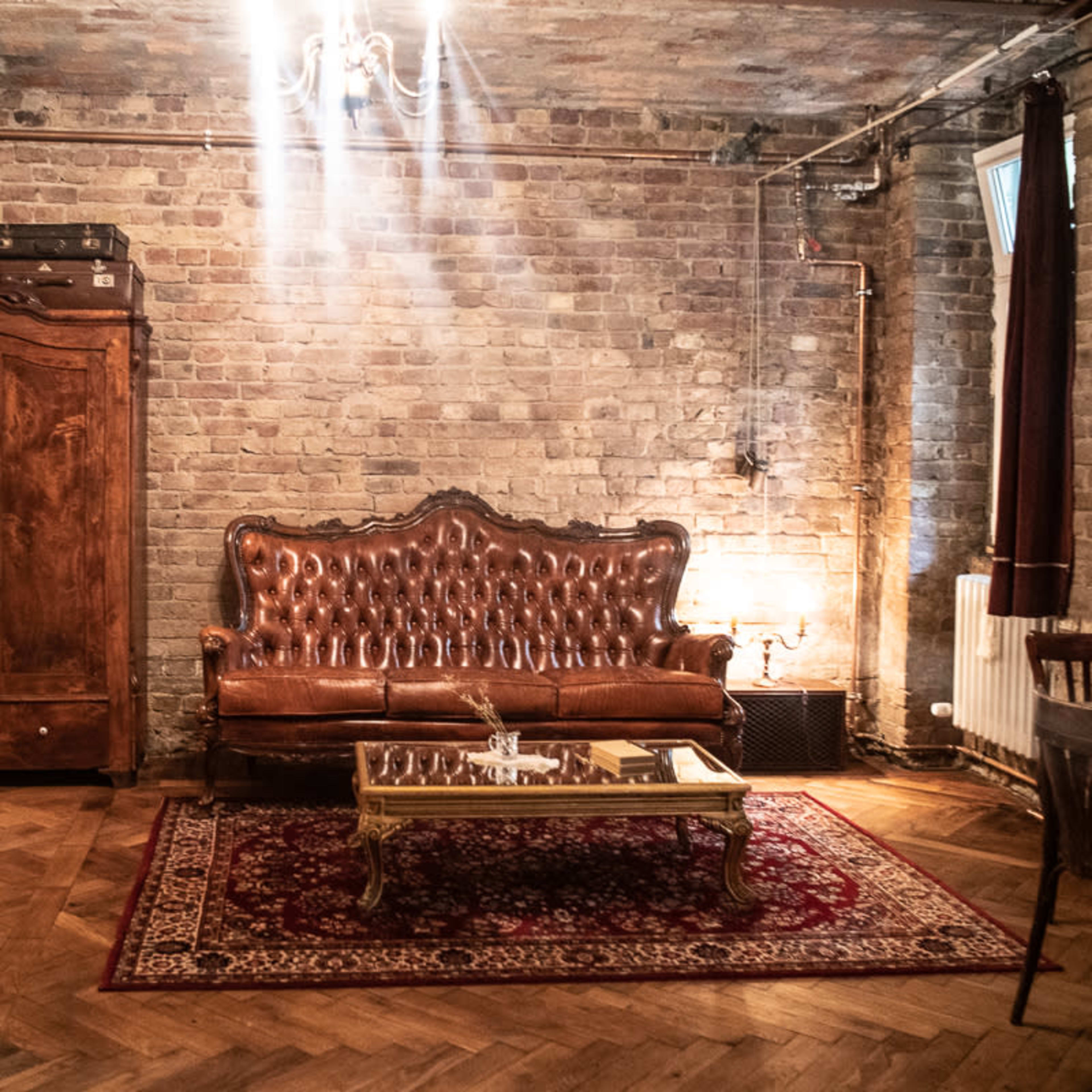 A rustic room with exposed brick walls, featuring a vintage leather sofa and a wooden armoire, illuminated by soft lighting.