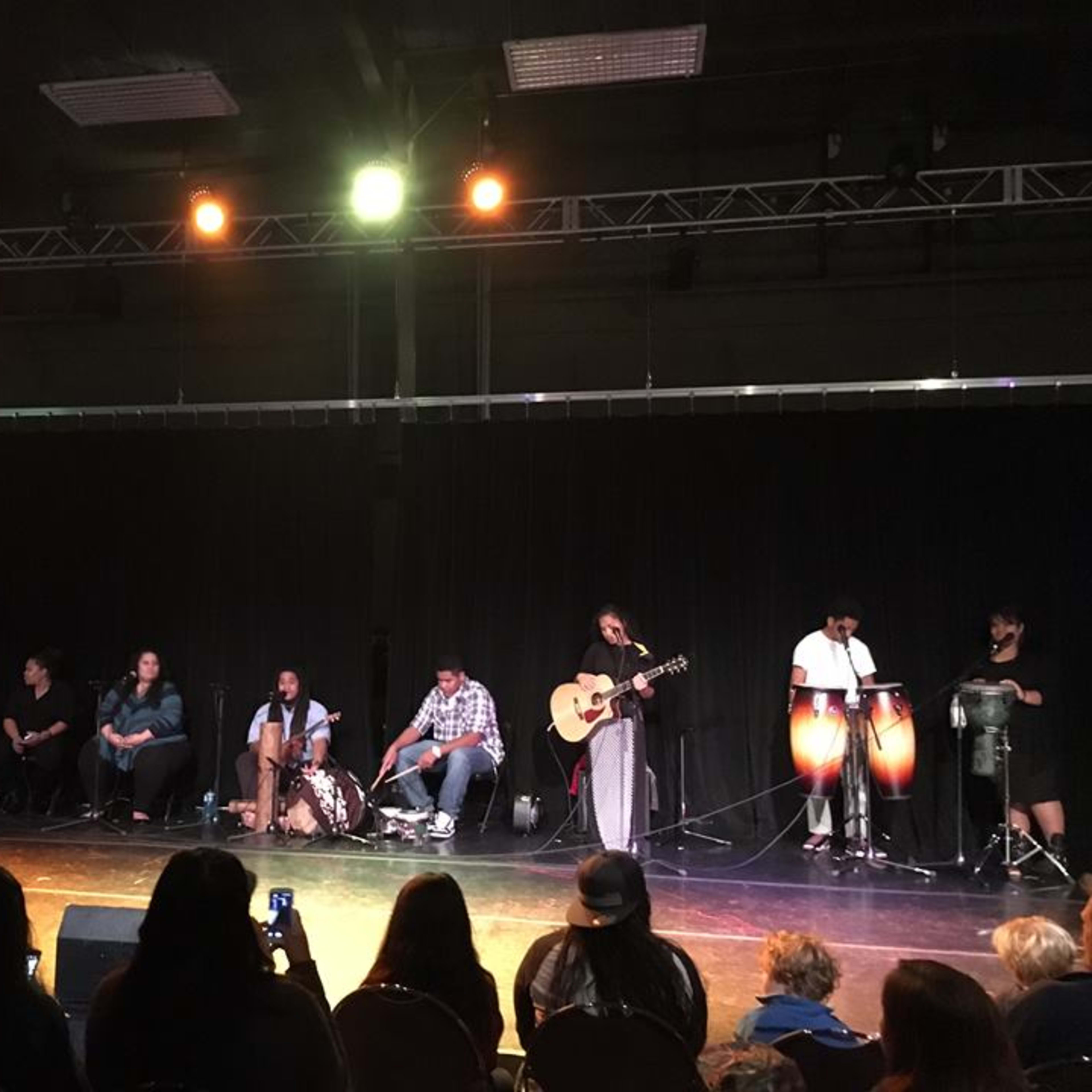A group of musicians plays instruments on stage in a dimly lit performance space.
