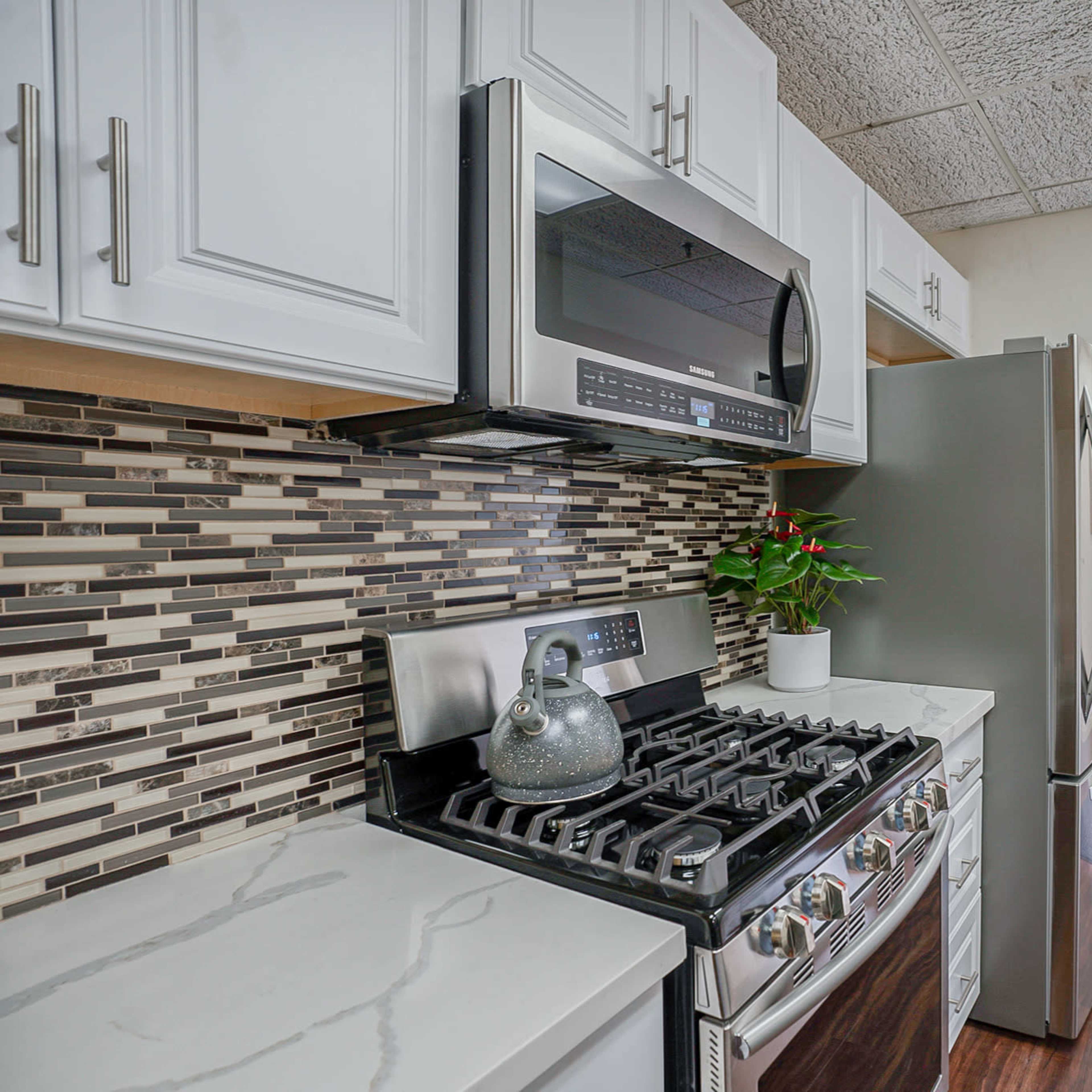 This image shows a kitchen with white cabinetry, stainless steel appliances, a gas stove, and a tiled backsplash.