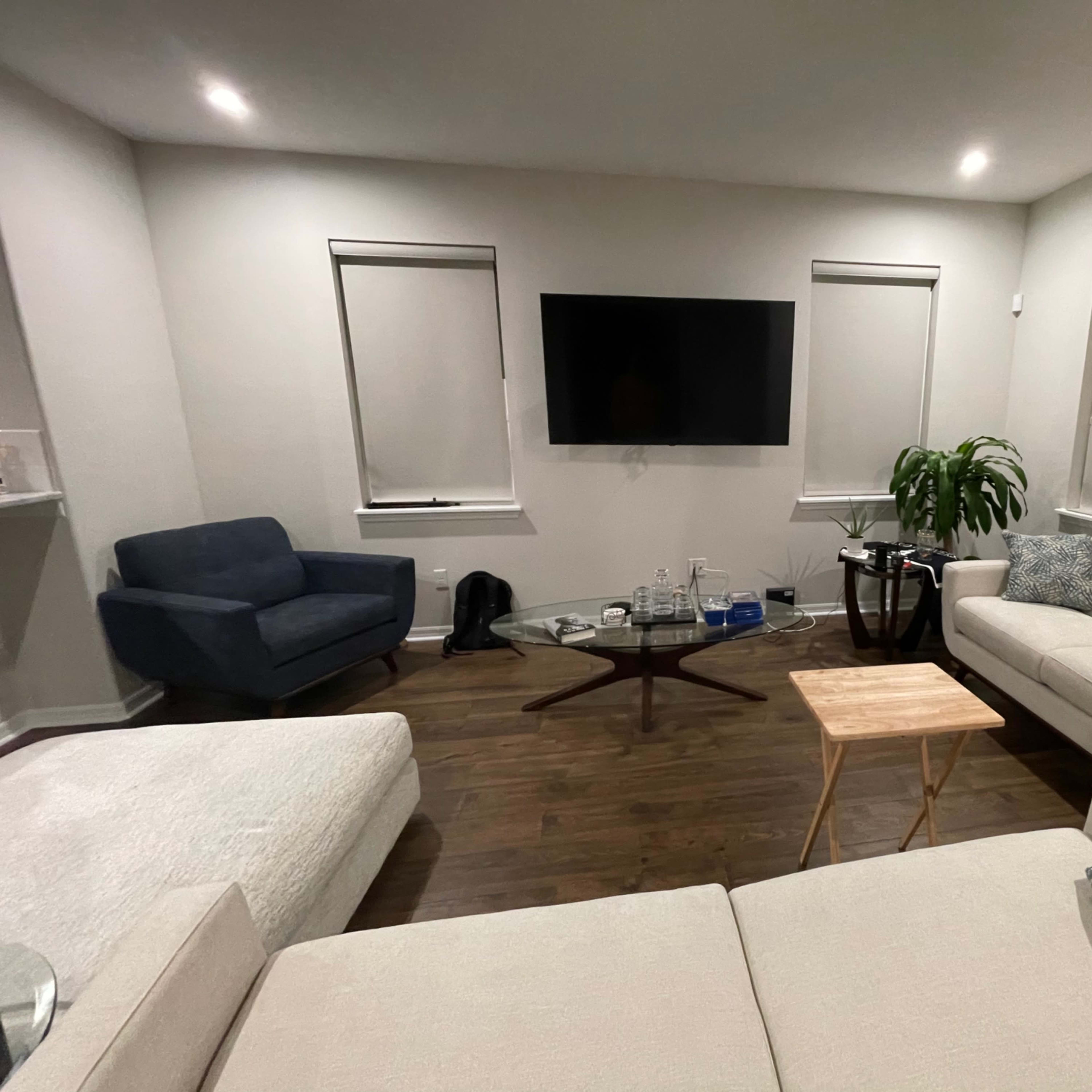 A modern living room with a sectional sofa, an armchair, a coffee table, a television mounted on the wall, and a potted plant.