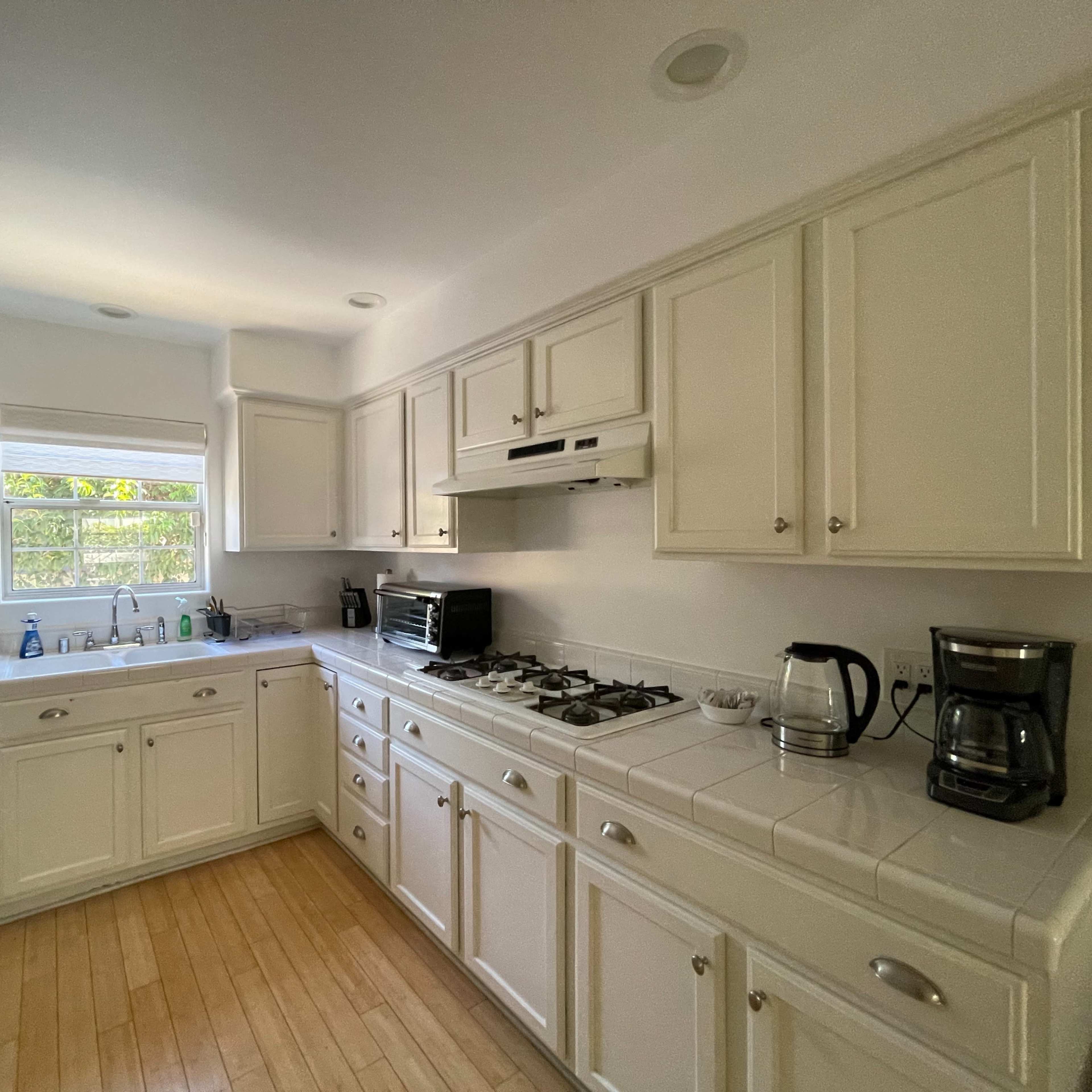A clean, modern kitchen features white cabinetry, a gas stove, and a coffee maker, with natural light streaming through a window.