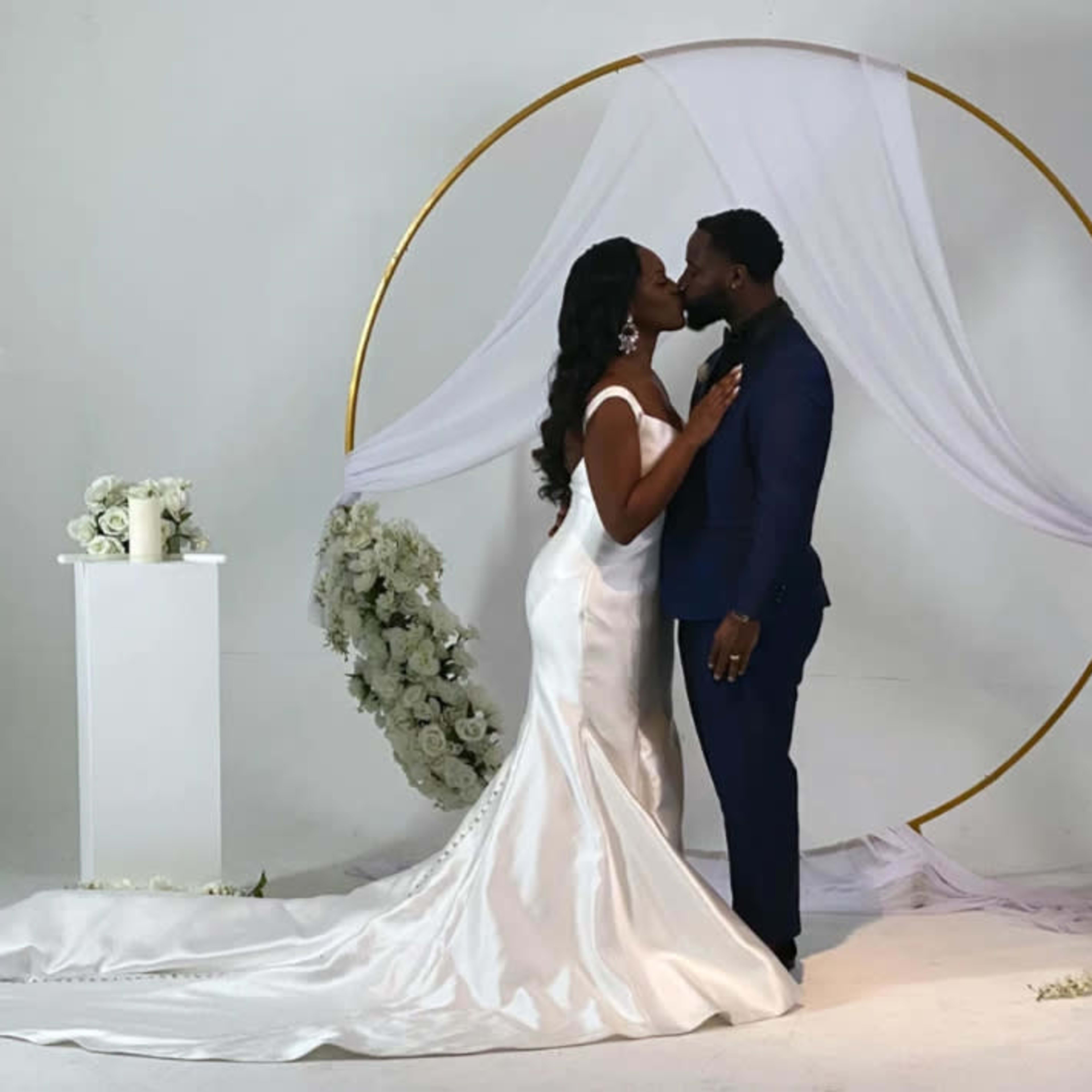 A bride and groom kiss in front of a circular floral archway at a wedding ceremony.