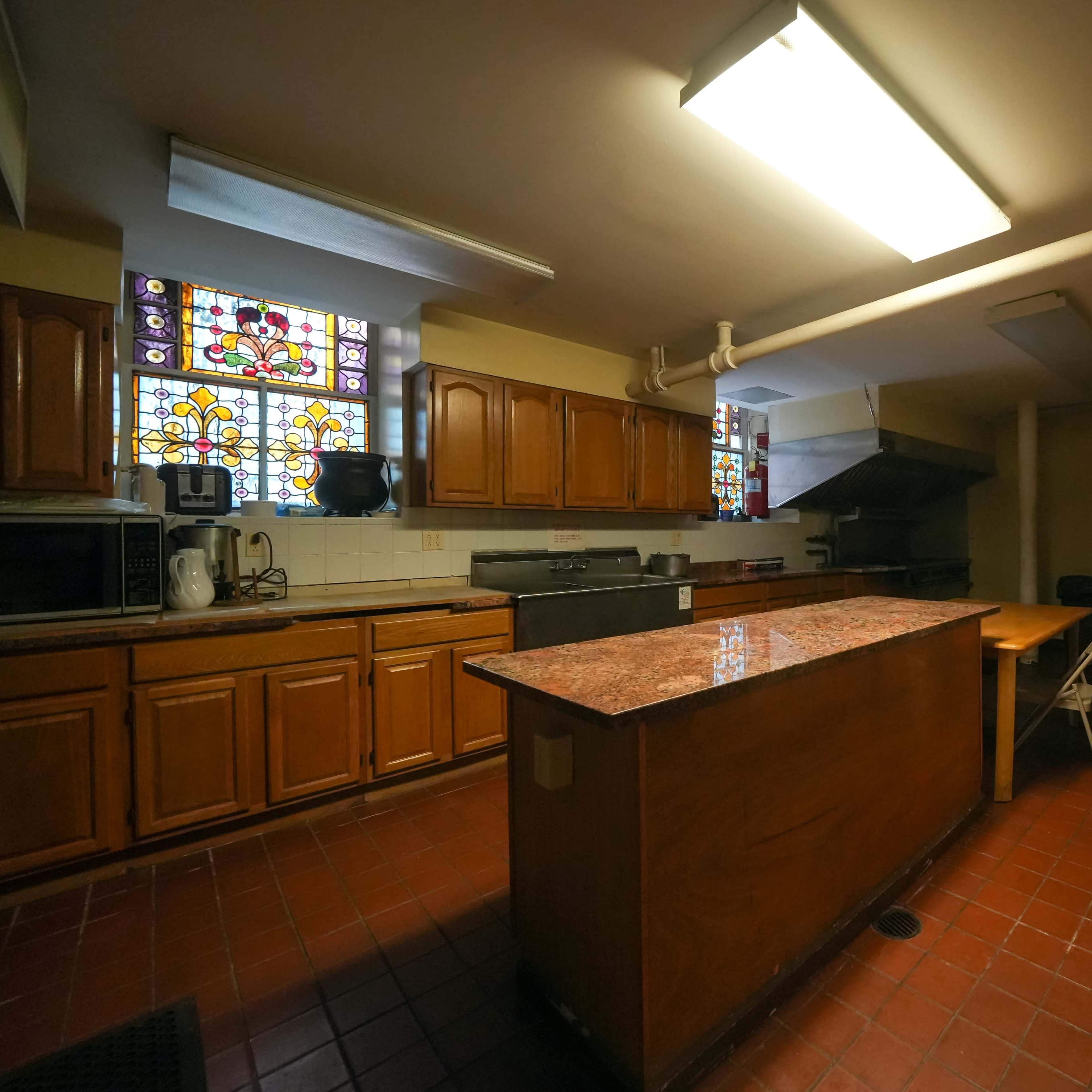A kitchen with wooden cabinets, a central island, stained glass windows, and various appliances.