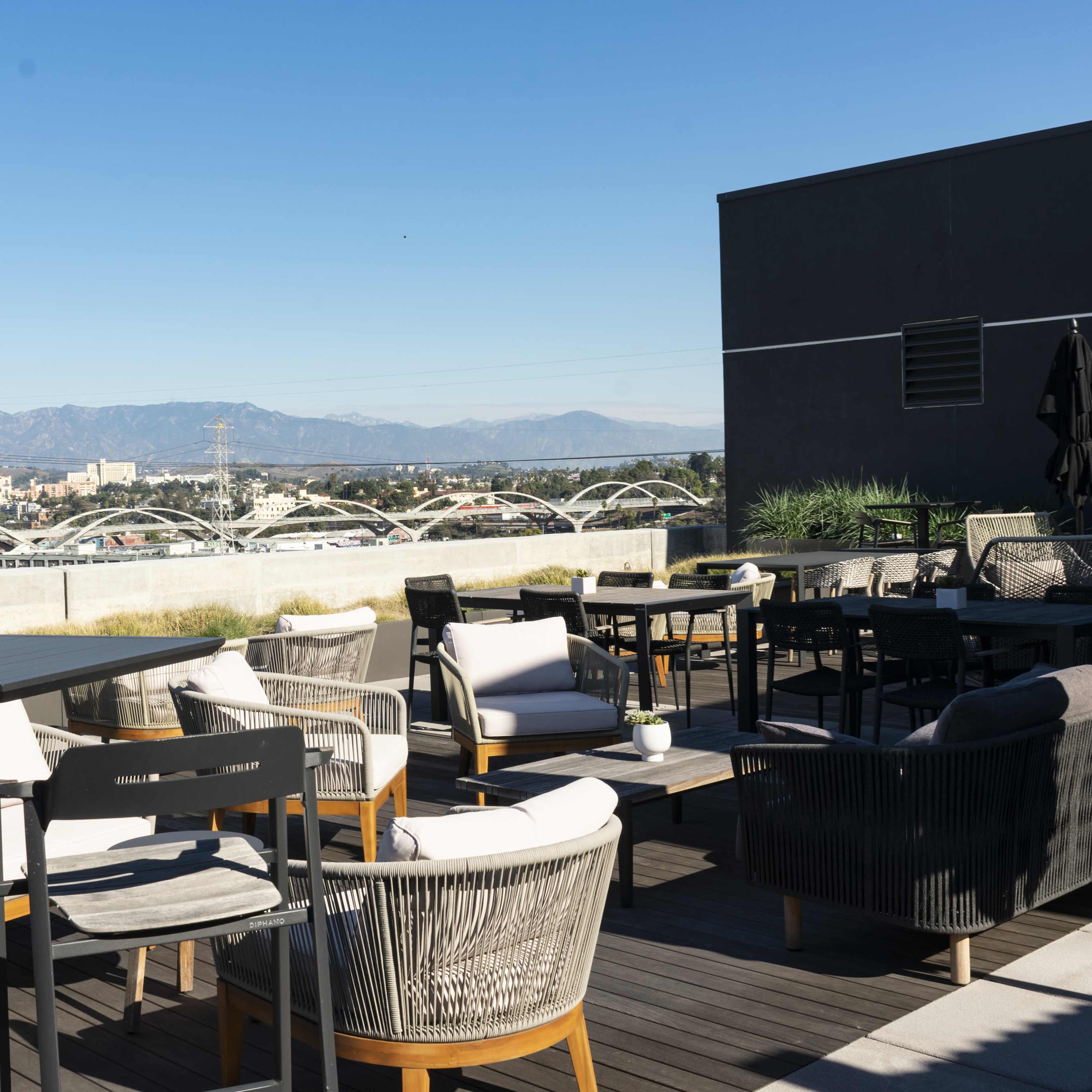 A rooftop terrace with various seating options and a view of mountains and a cityscape in the background.