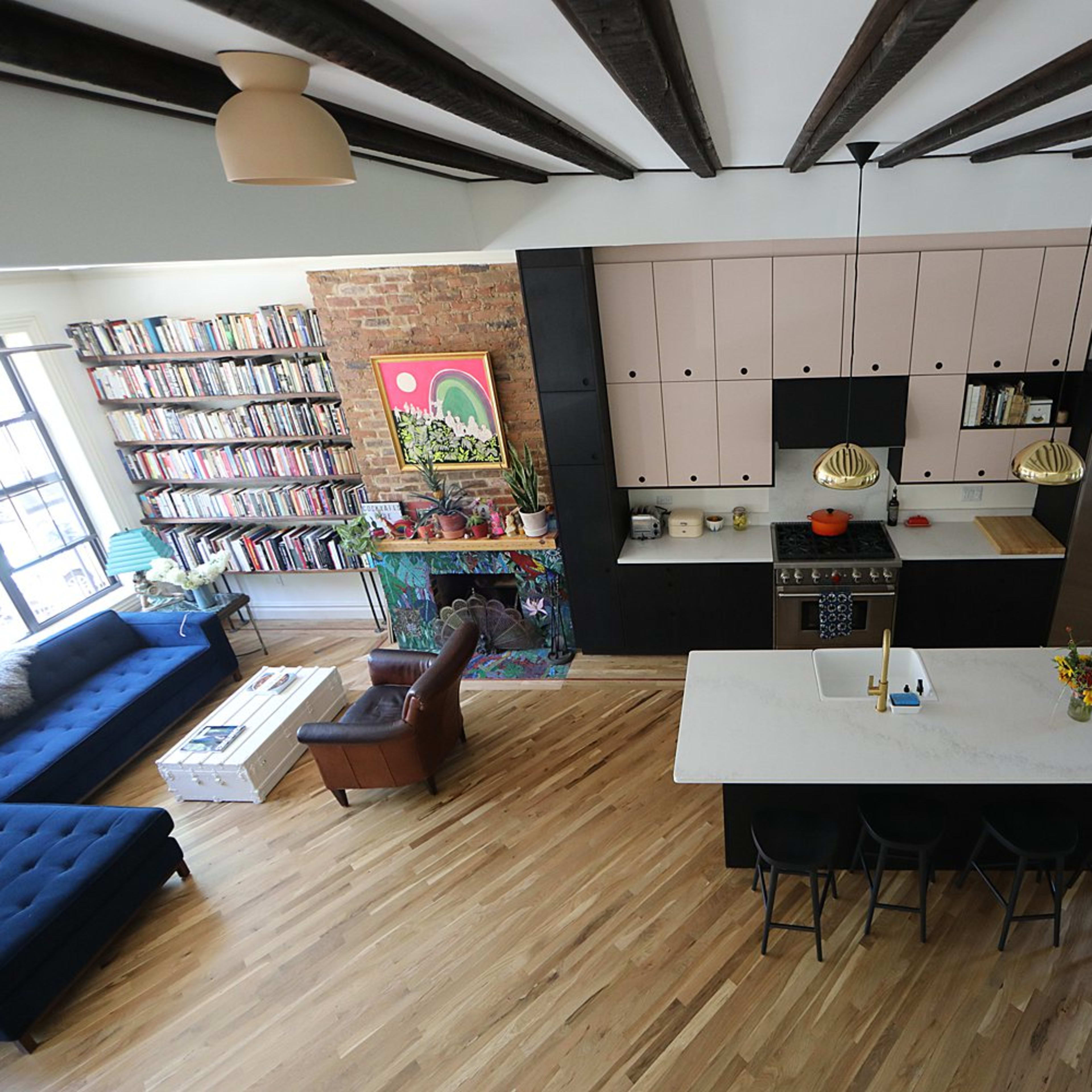 A modern open-concept kitchen and living area with hardwood flooring, featuring a large island, a blue sofa, and a library wall filled with books.