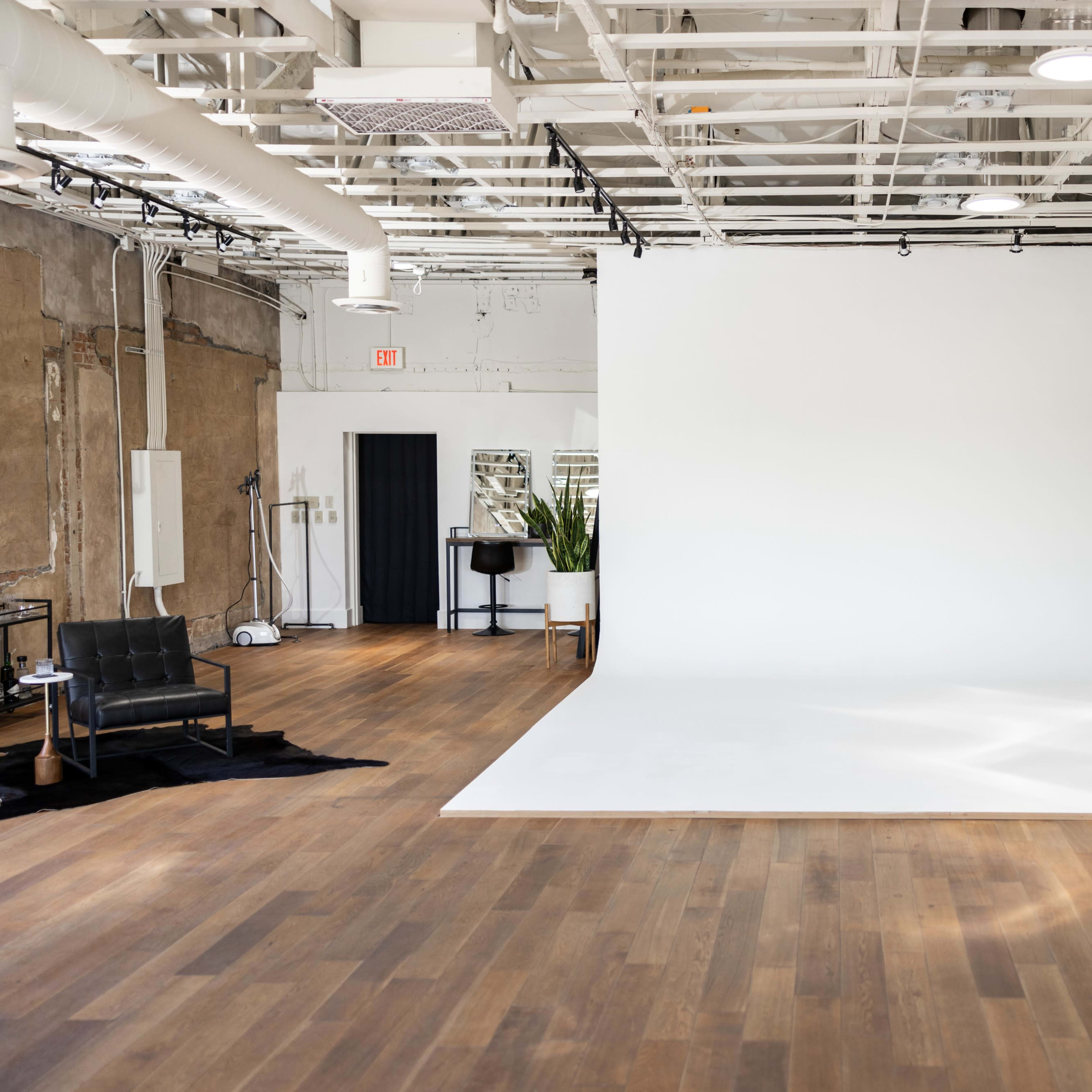 A spacious photography studio with a large white backdrop, wooden flooring, and minimal furniture.