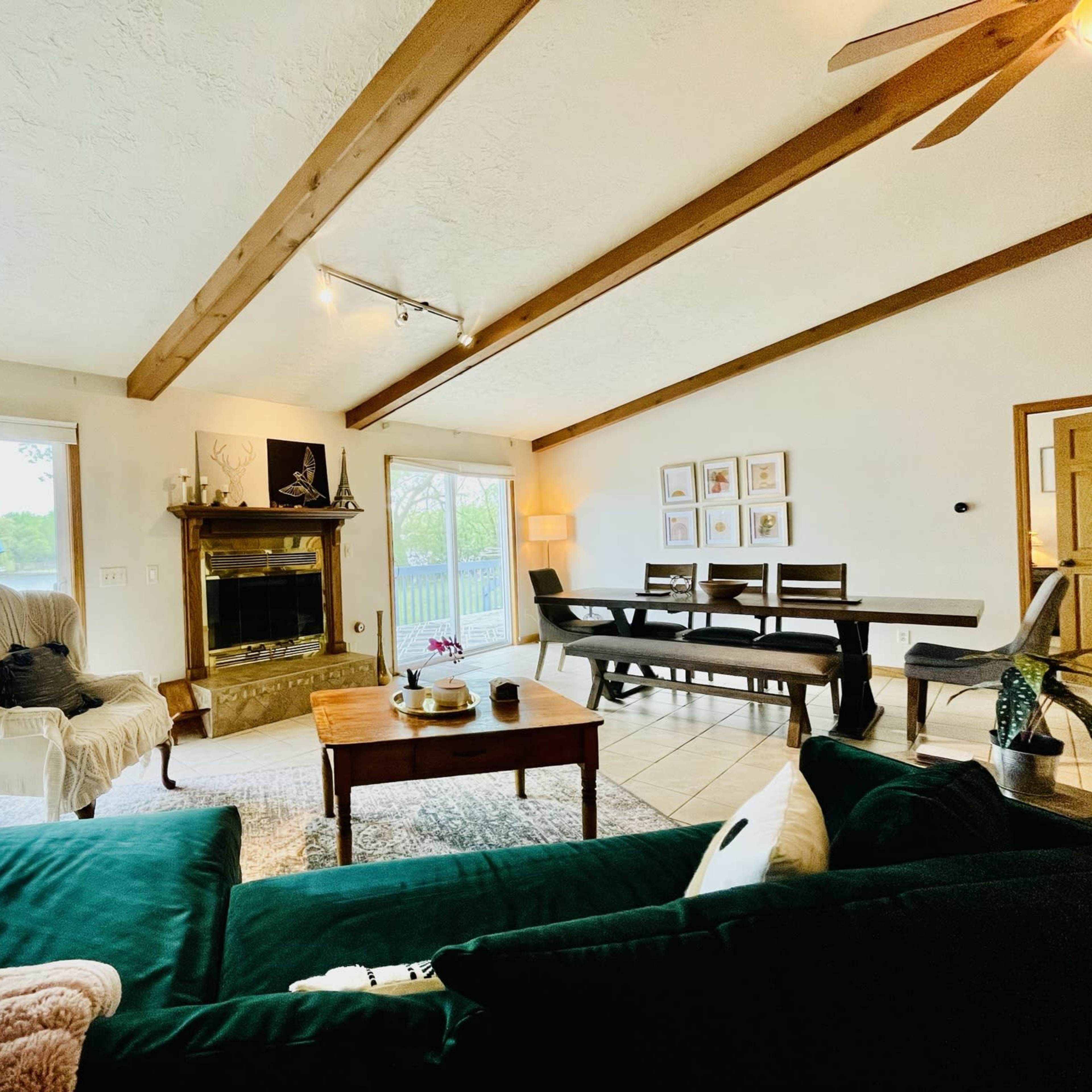 The living room features a sofa, a coffee table, a fireplace with a mantel, and dining space with sliding glass doors opening to a deck.