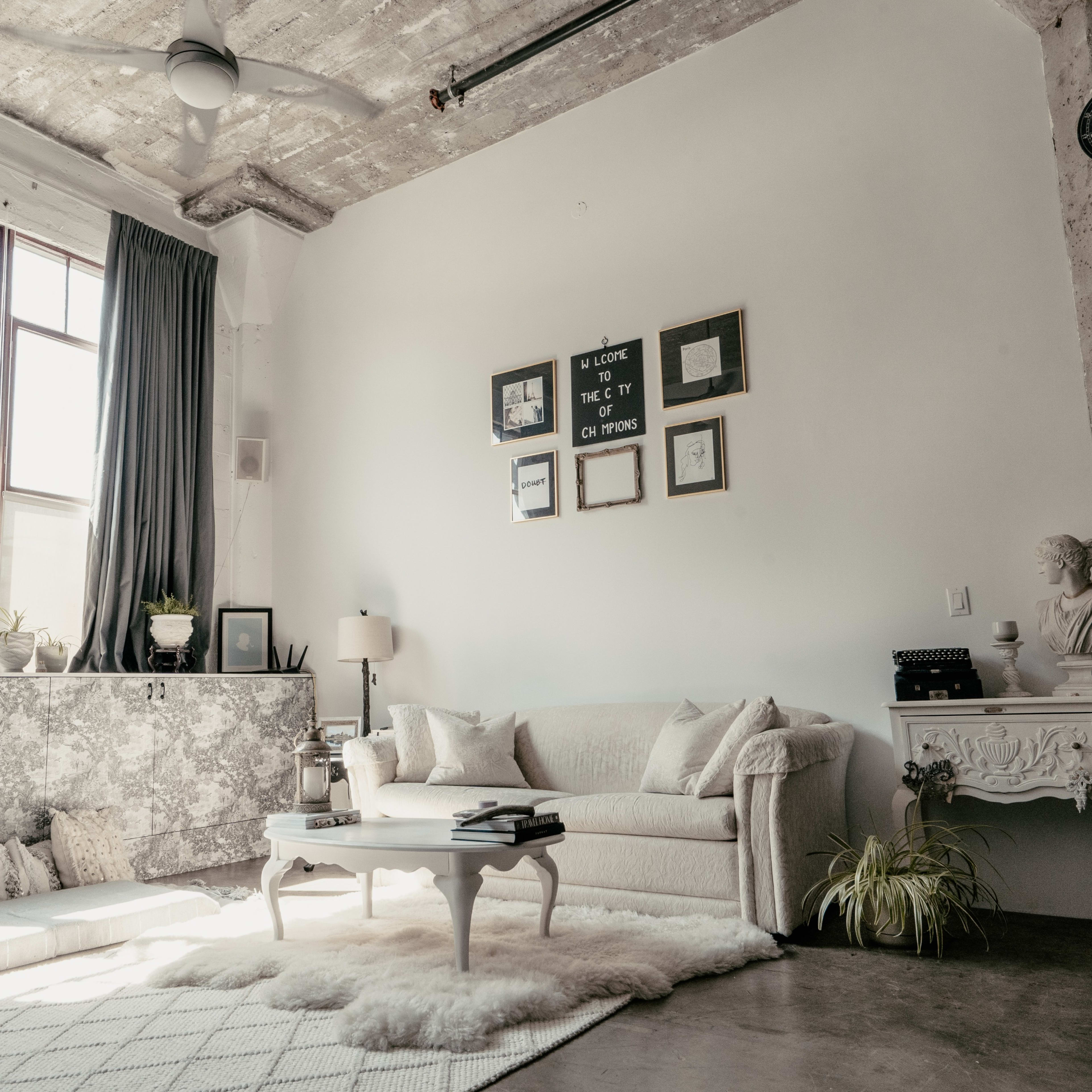 A modern living room with a light-colored sofa, a coffee table, and large windows allowing natural light to enter the space.