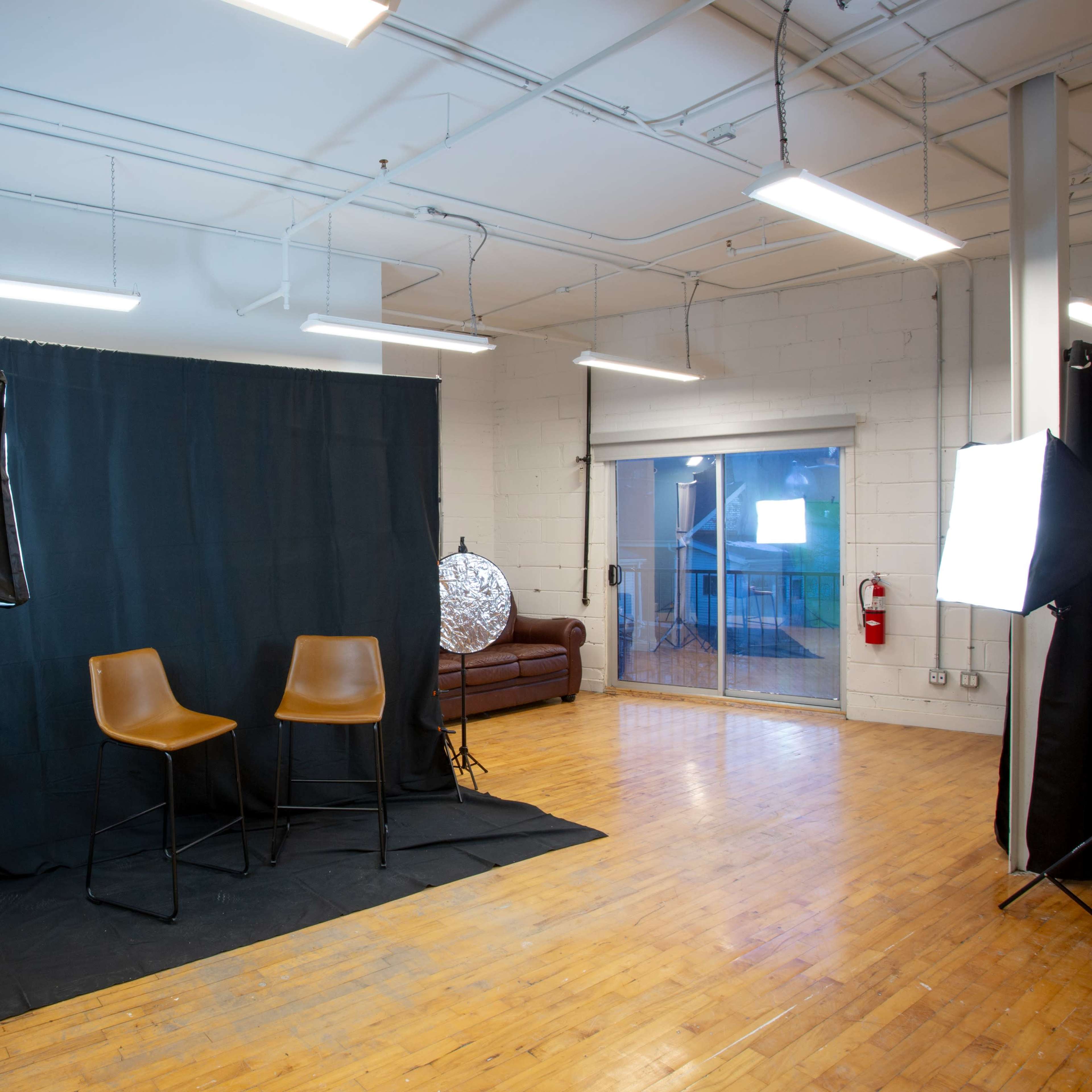 A studio setup with two brown chairs on a black mat, green and black backdrops, and lighting equipment arranged around the space.