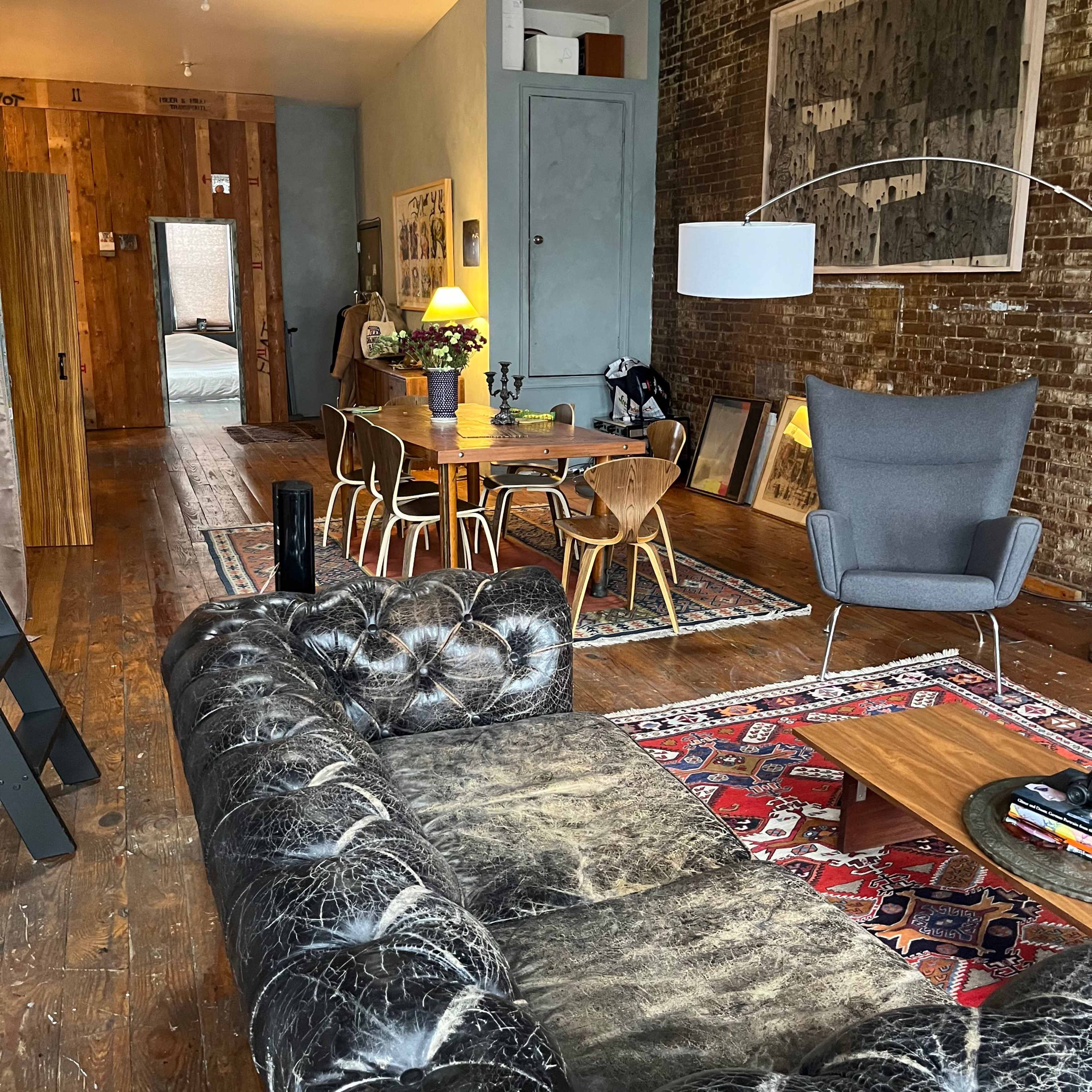 A stylish living space featuring a leather sofa, a wooden dining table with chairs, and exposed brick walls.