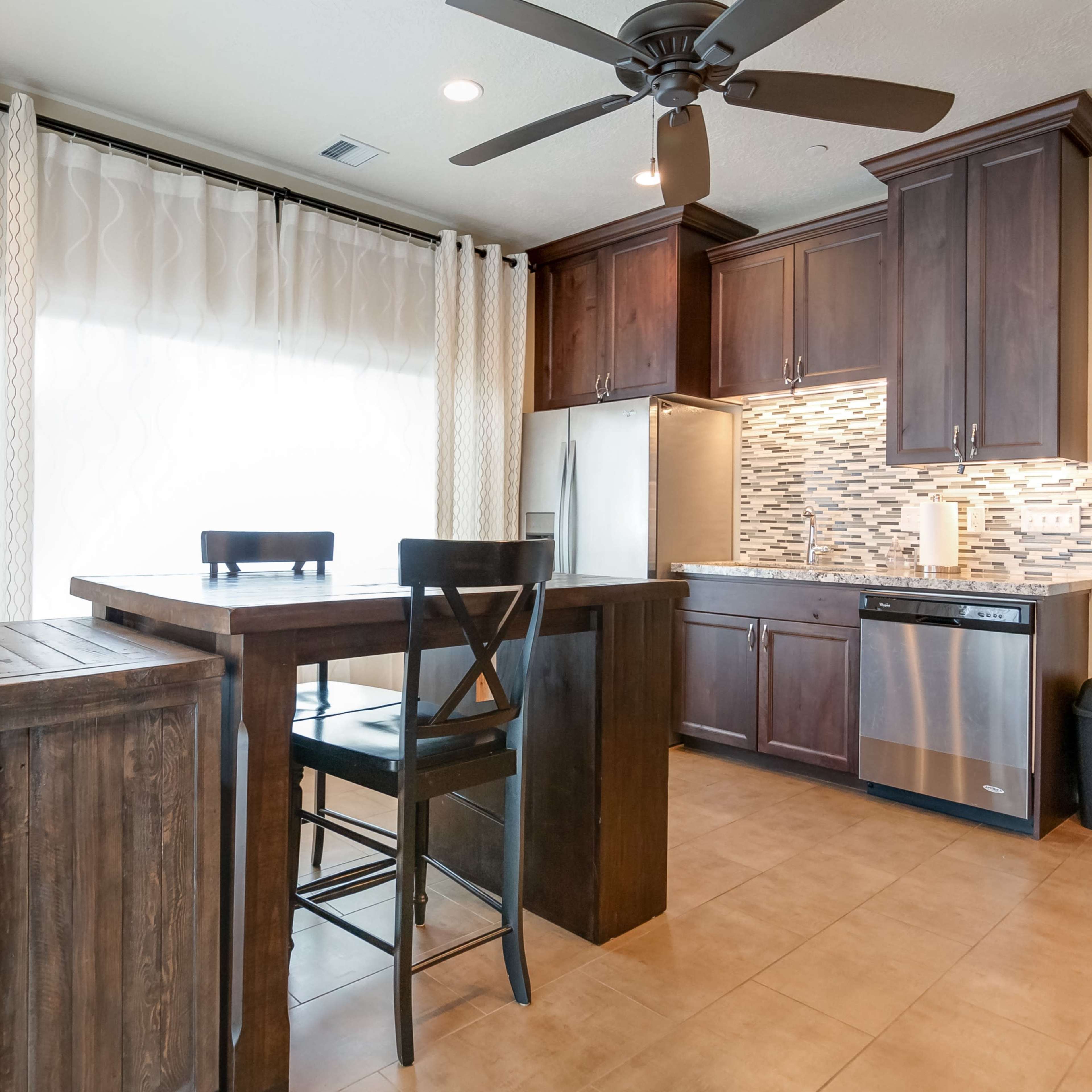 A modern kitchen features dark wooden cabinets, a tiled backsplash, and a small dining table with two black chairs.
