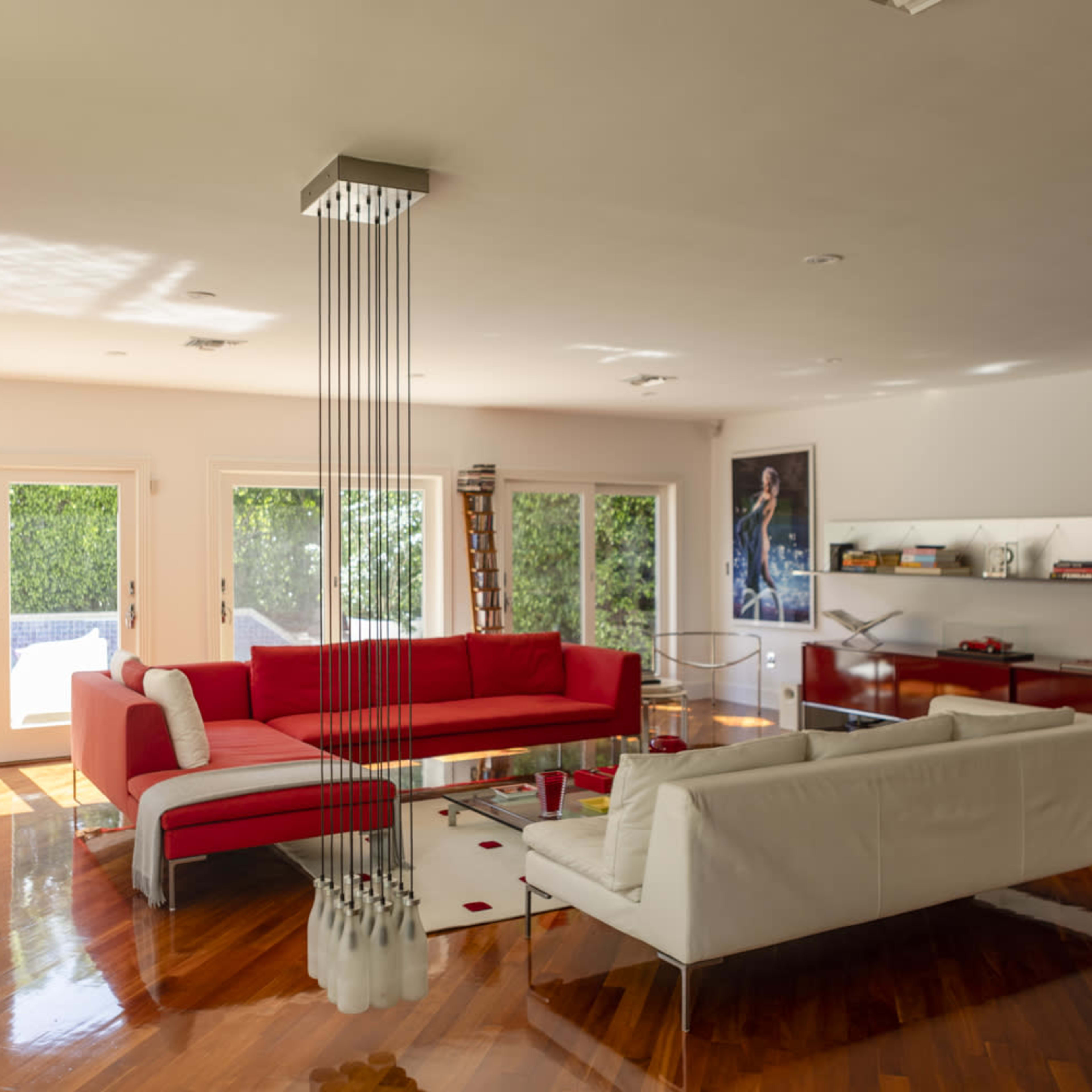 A modern living room with red and white sofas, large windows, and polished wooden floors.