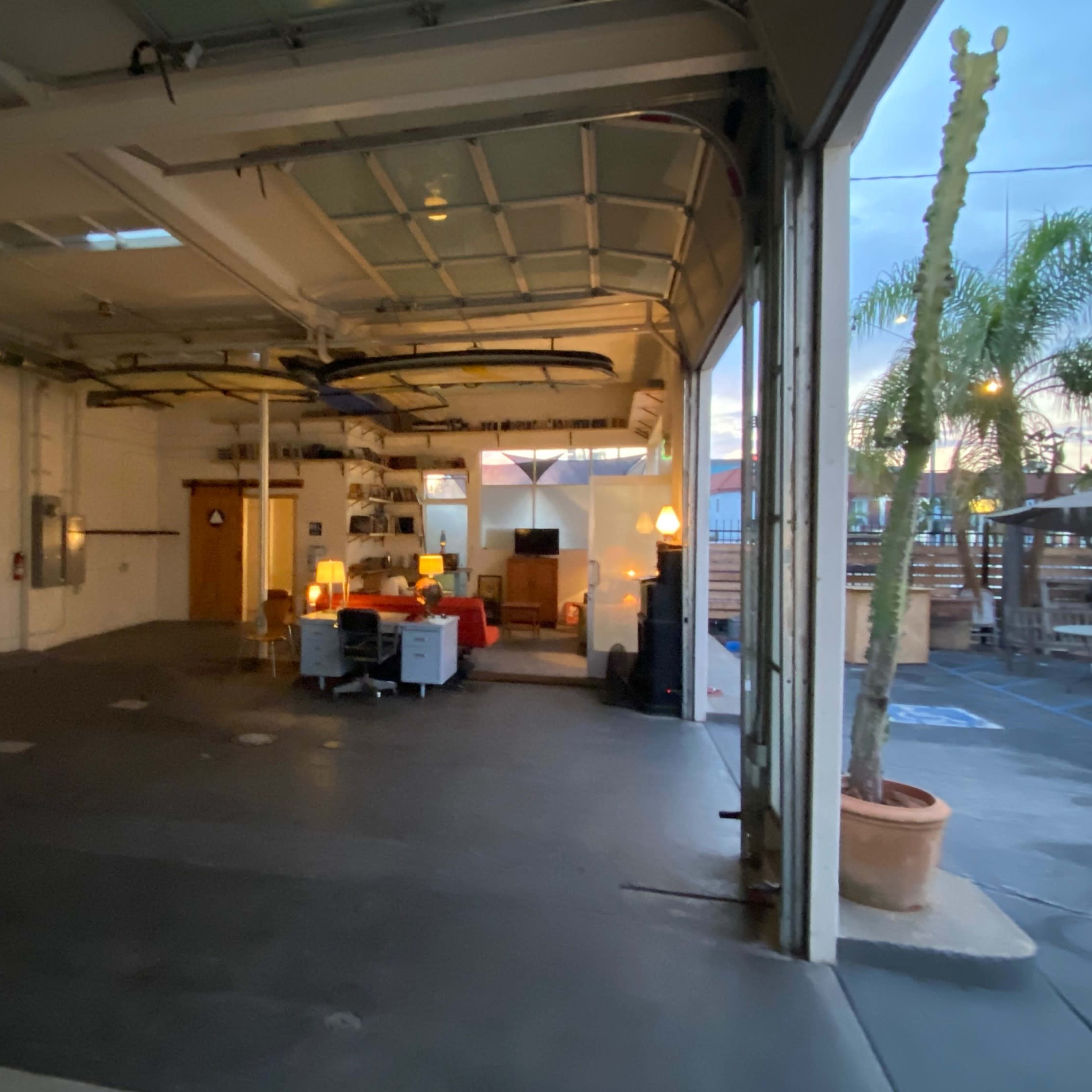An empty garage space with a sitting area and potted palm trees visible outside.