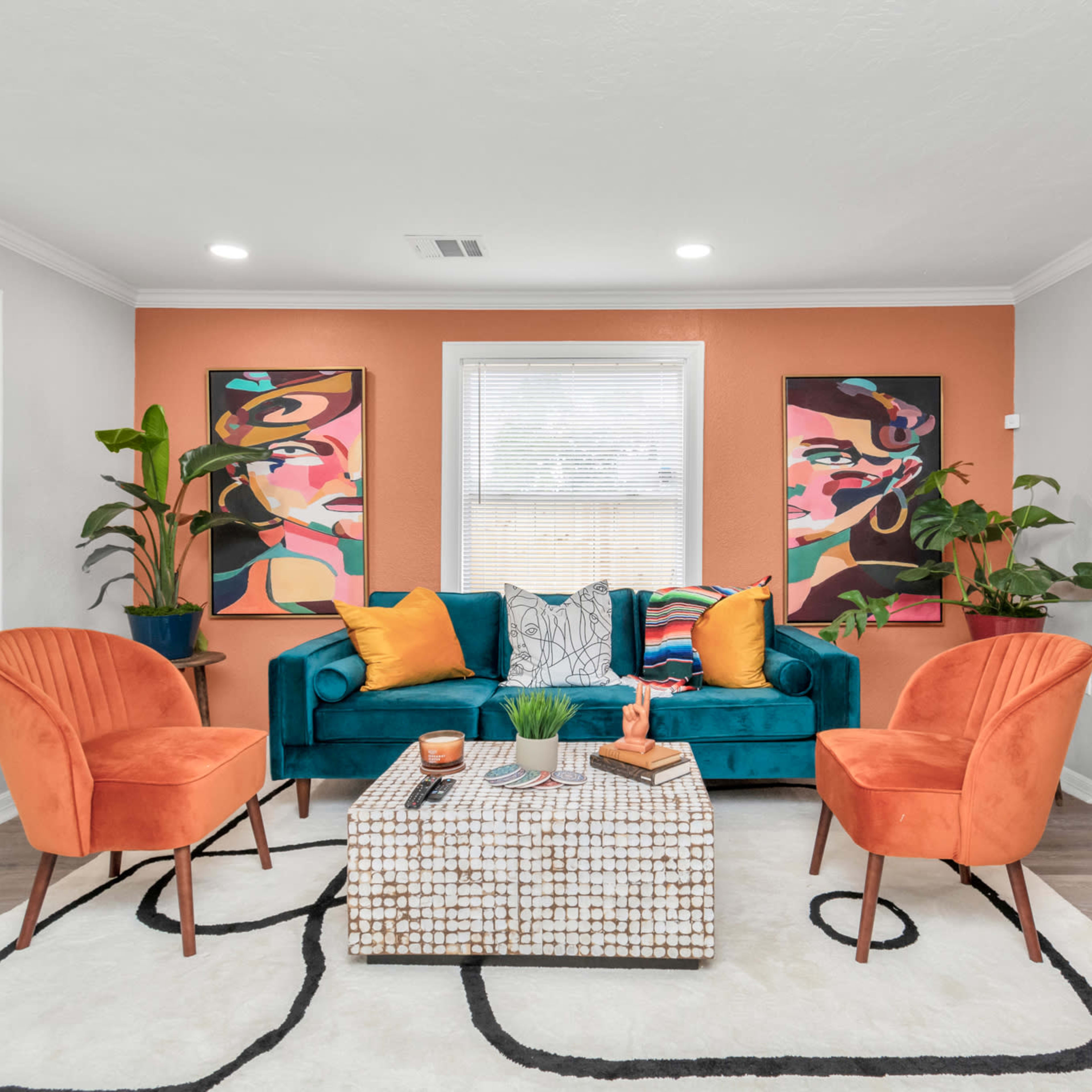The living room features a teal sofa, two orange chairs, a patterned rug, and vibrant artwork on the walls.