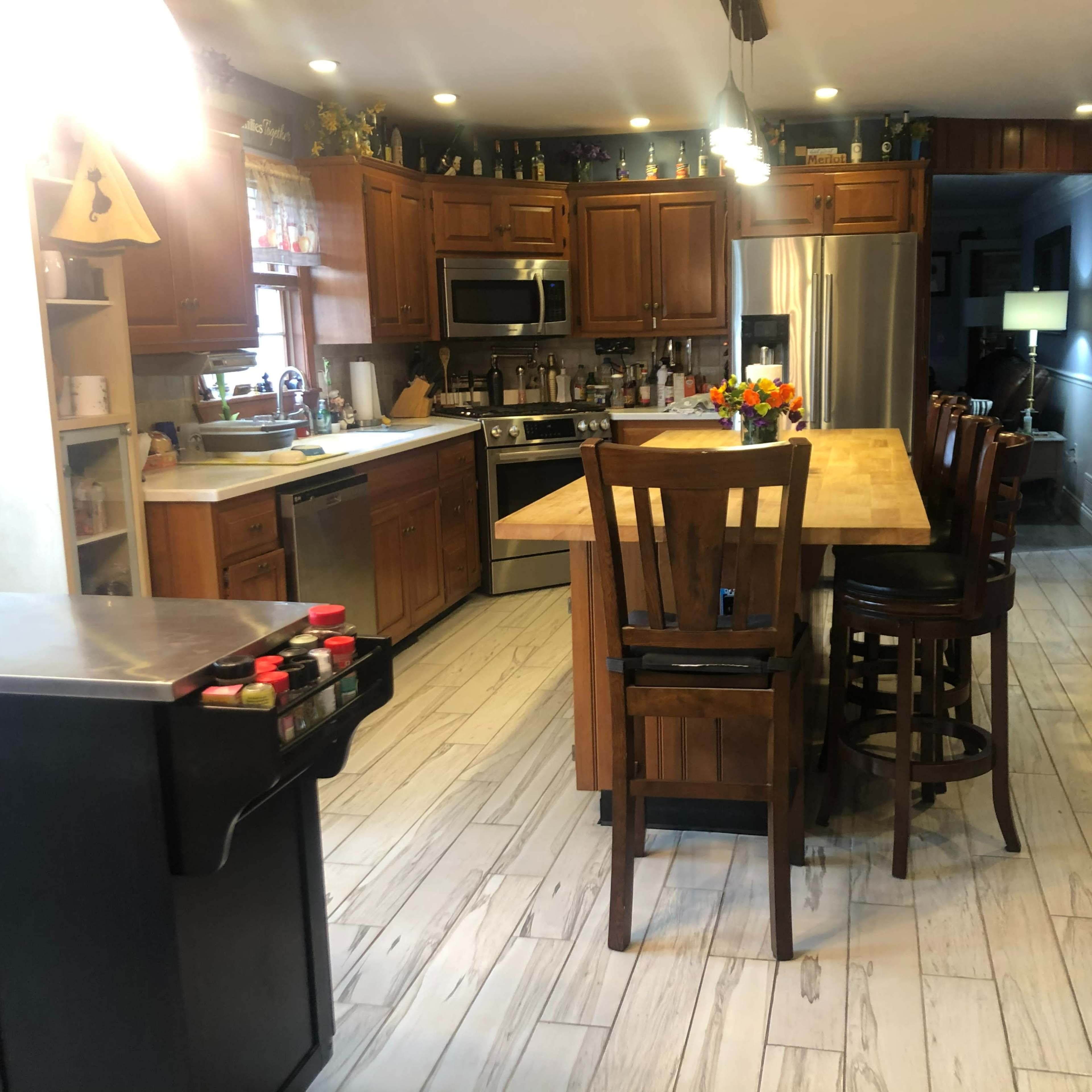 A spacious kitchen with wooden cabinets, an island with seating, stainless steel appliances, and a tile floor.