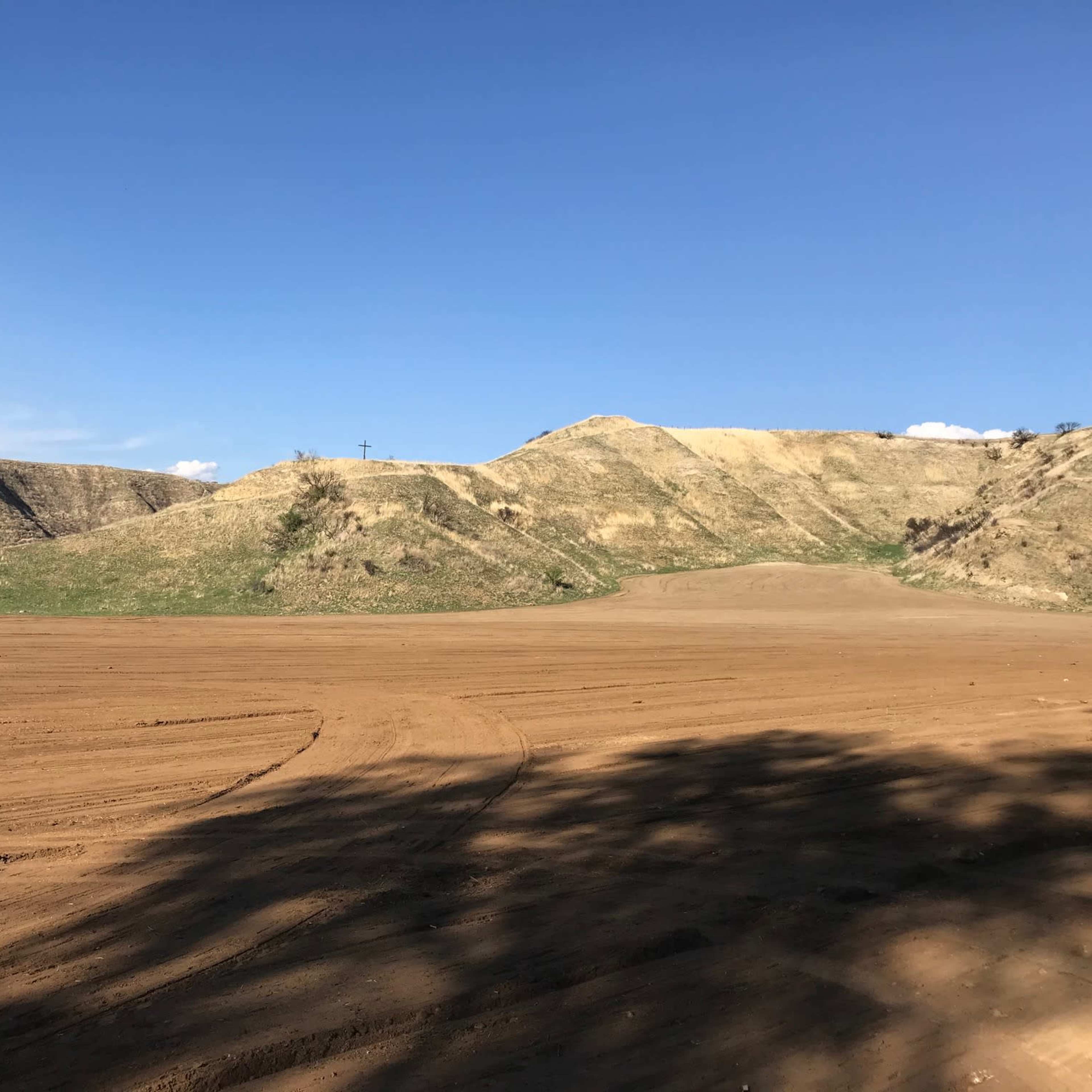 A flat, bare landscape stretches out with rolling hills in the background under a clear blue sky.