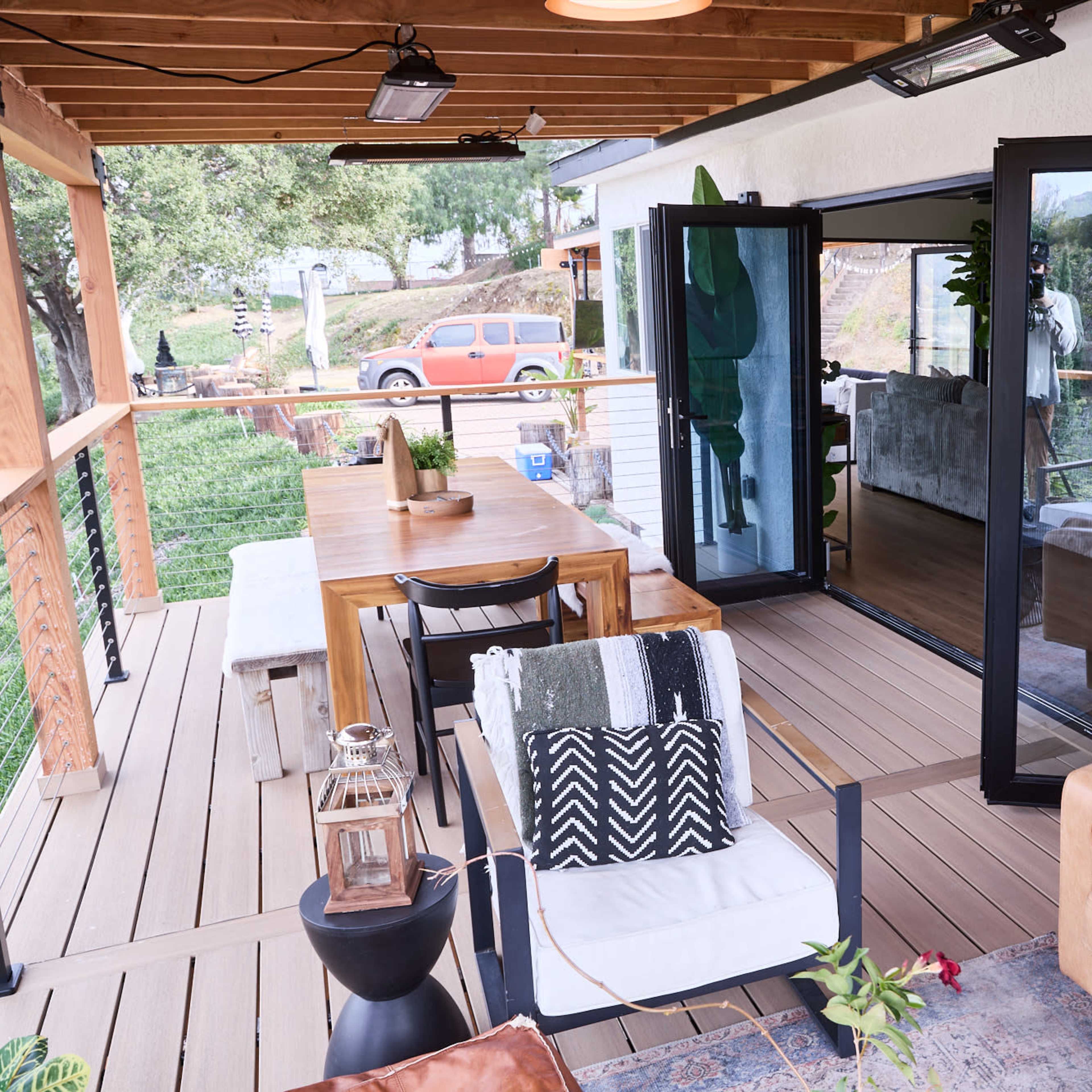 A modern outdoor seating area with a dining table, a sofa, and views of a landscape through glass doors.
