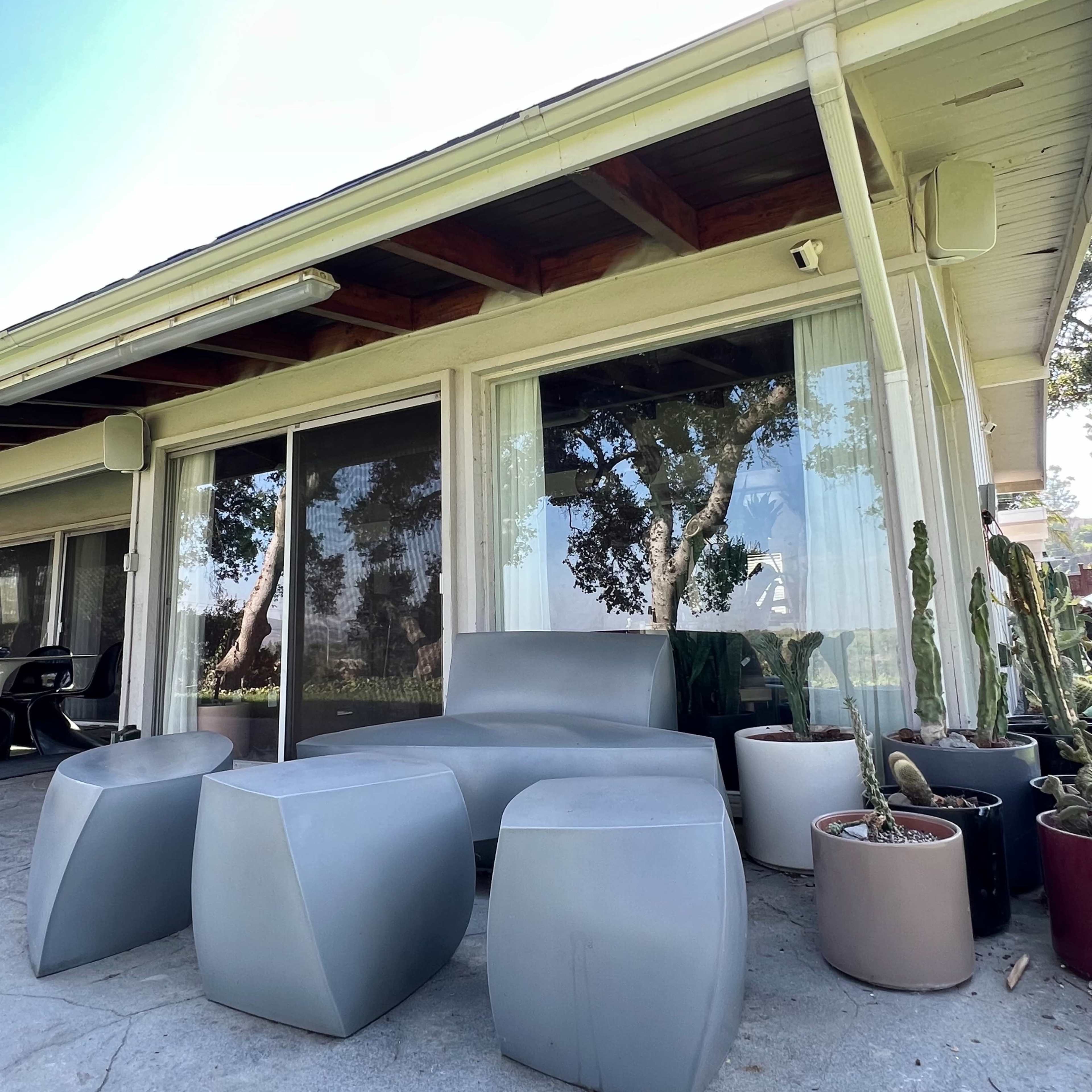 A modern outdoor seating area features geometric gray furniture and potted plants near a glass sliding door.