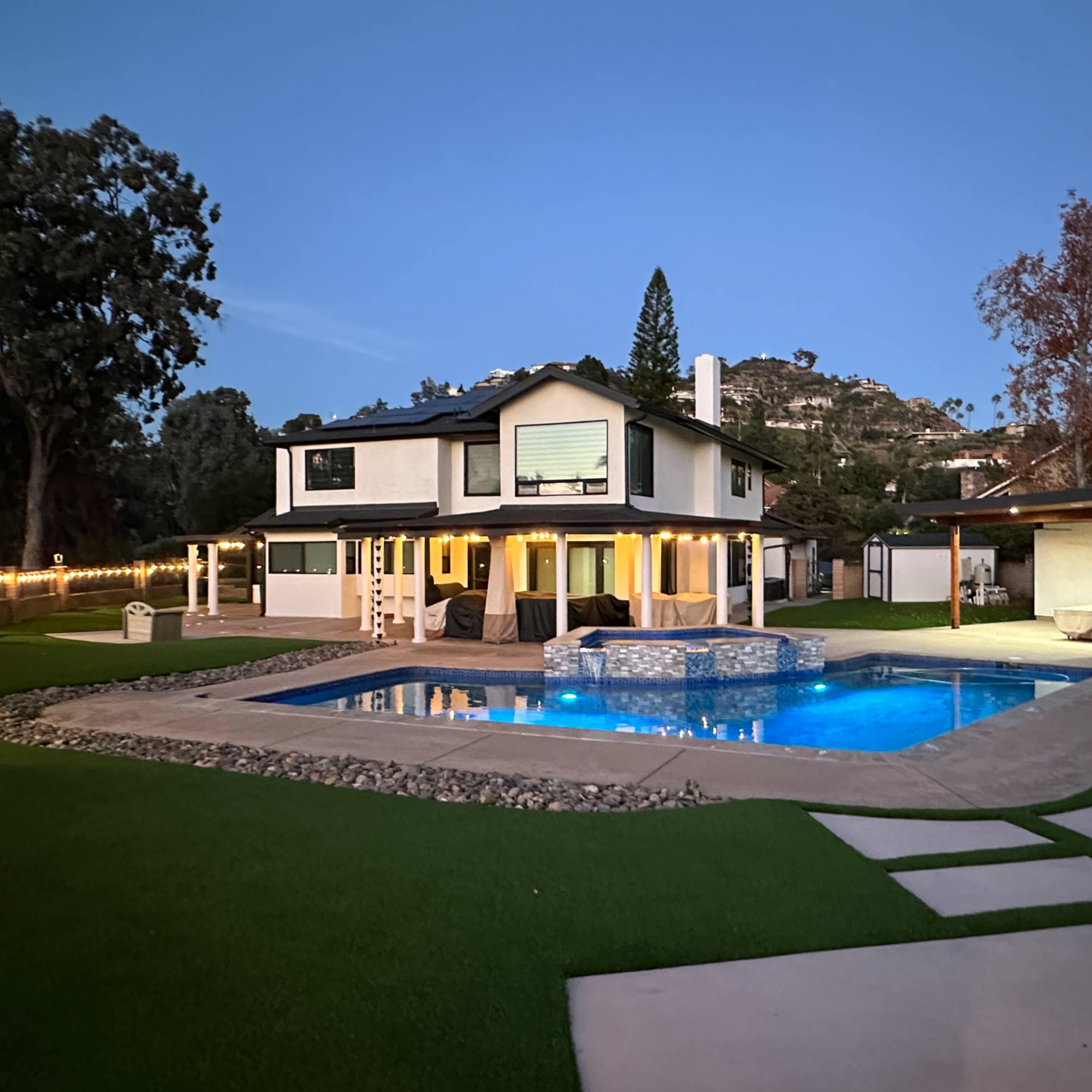 A two-story house with a pool surrounded by a landscaped yard at twilight.