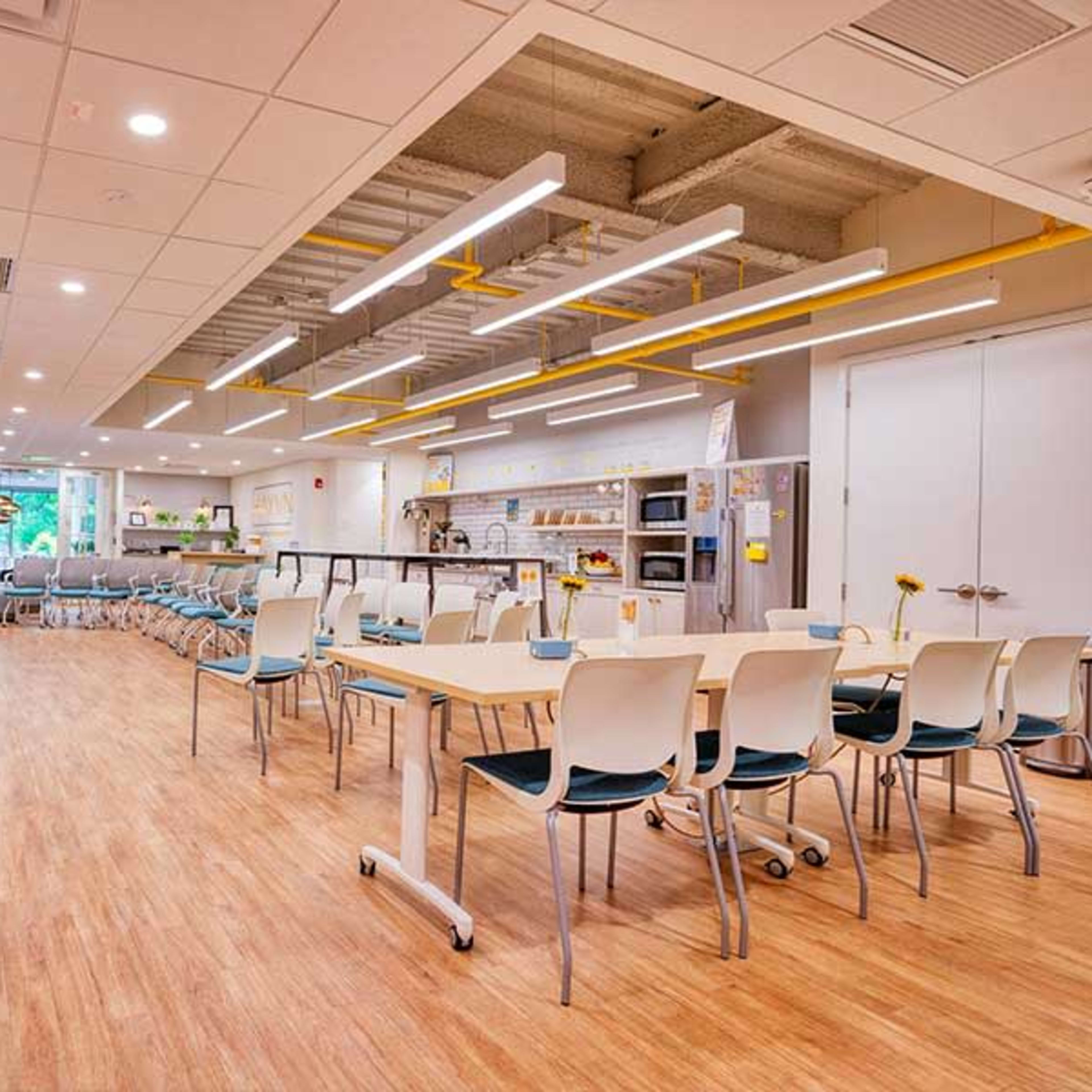 A modern, open space with tables and chairs arranged for dining or collaboration, featuring bright lighting and a cozy atmosphere.