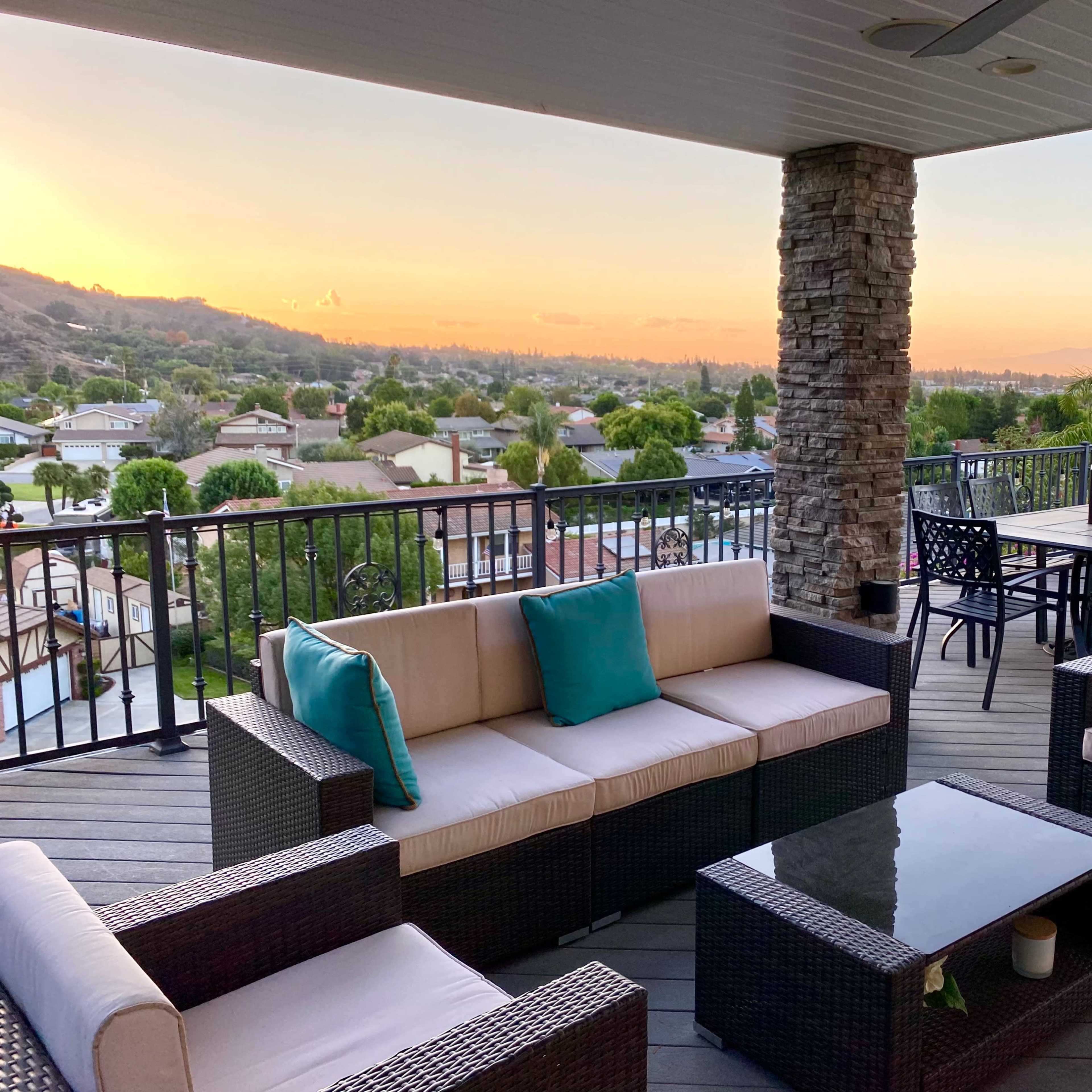 An outdoor patio area with seating, a table, and a view of a sunset over a suburban landscape.