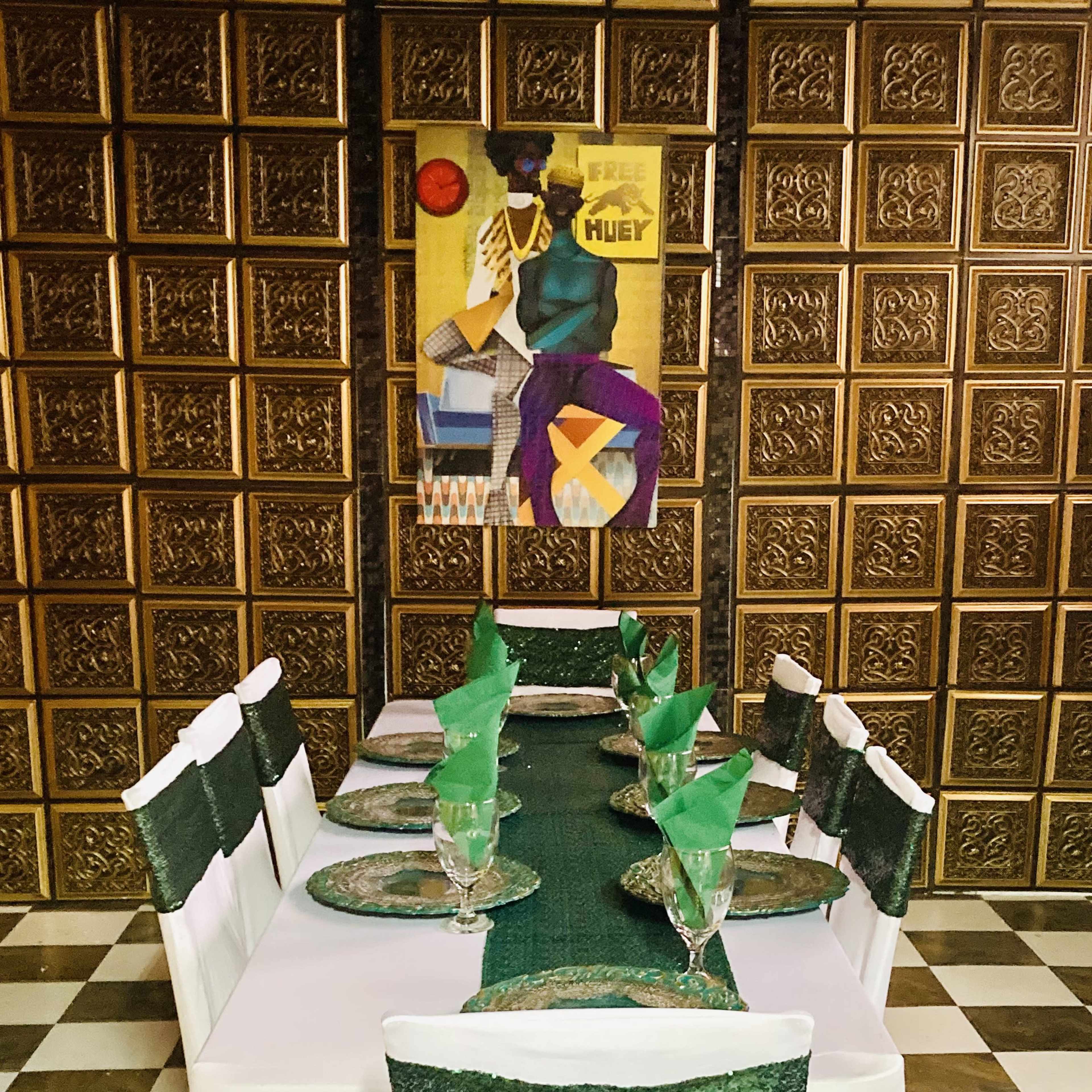 A dining table is set with green-themed decorations and a patterned wall in the background.