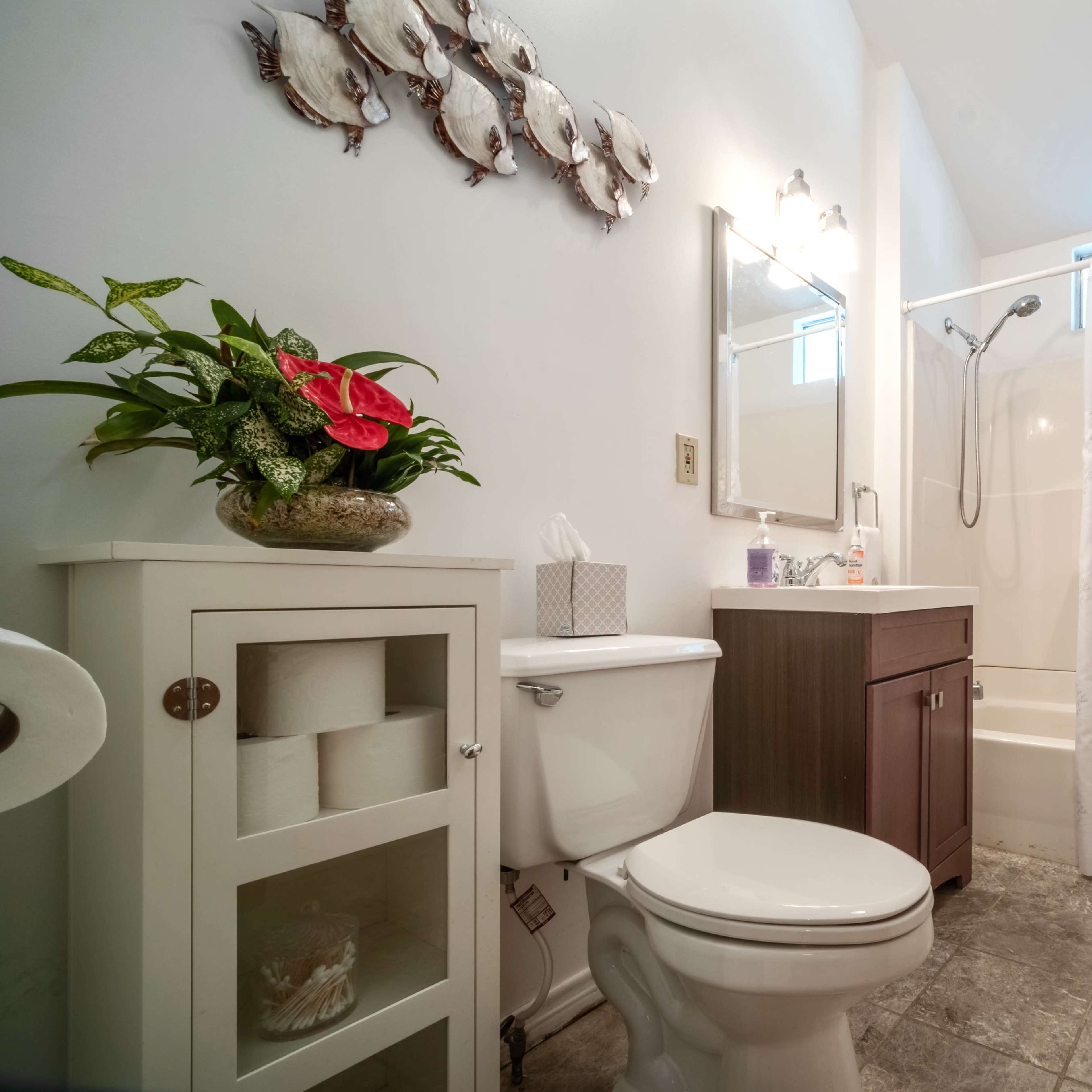 A clean bathroom featuring a shower with a curtain, a toilet, a sink with a cabinet, and decorative wall art.