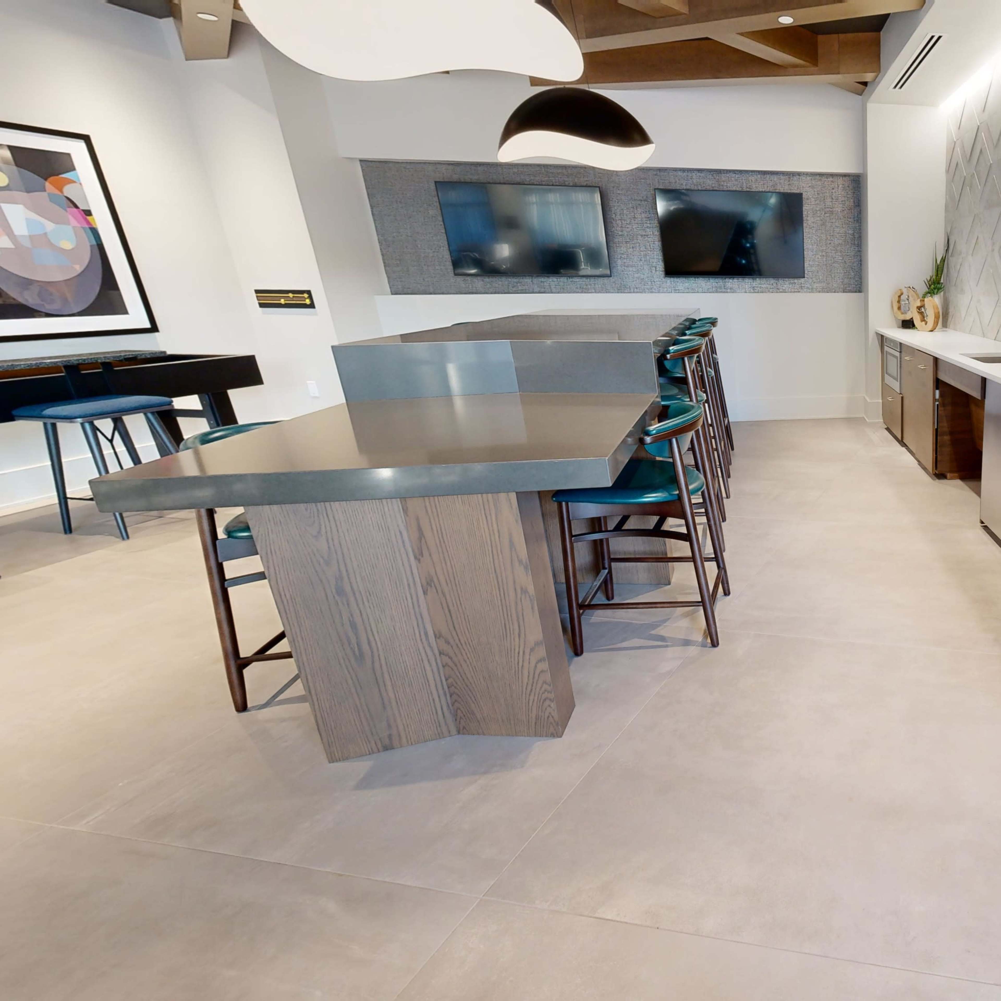 A modern kitchen area with a large island, bar stools, a sink, and two wall-mounted televisions.