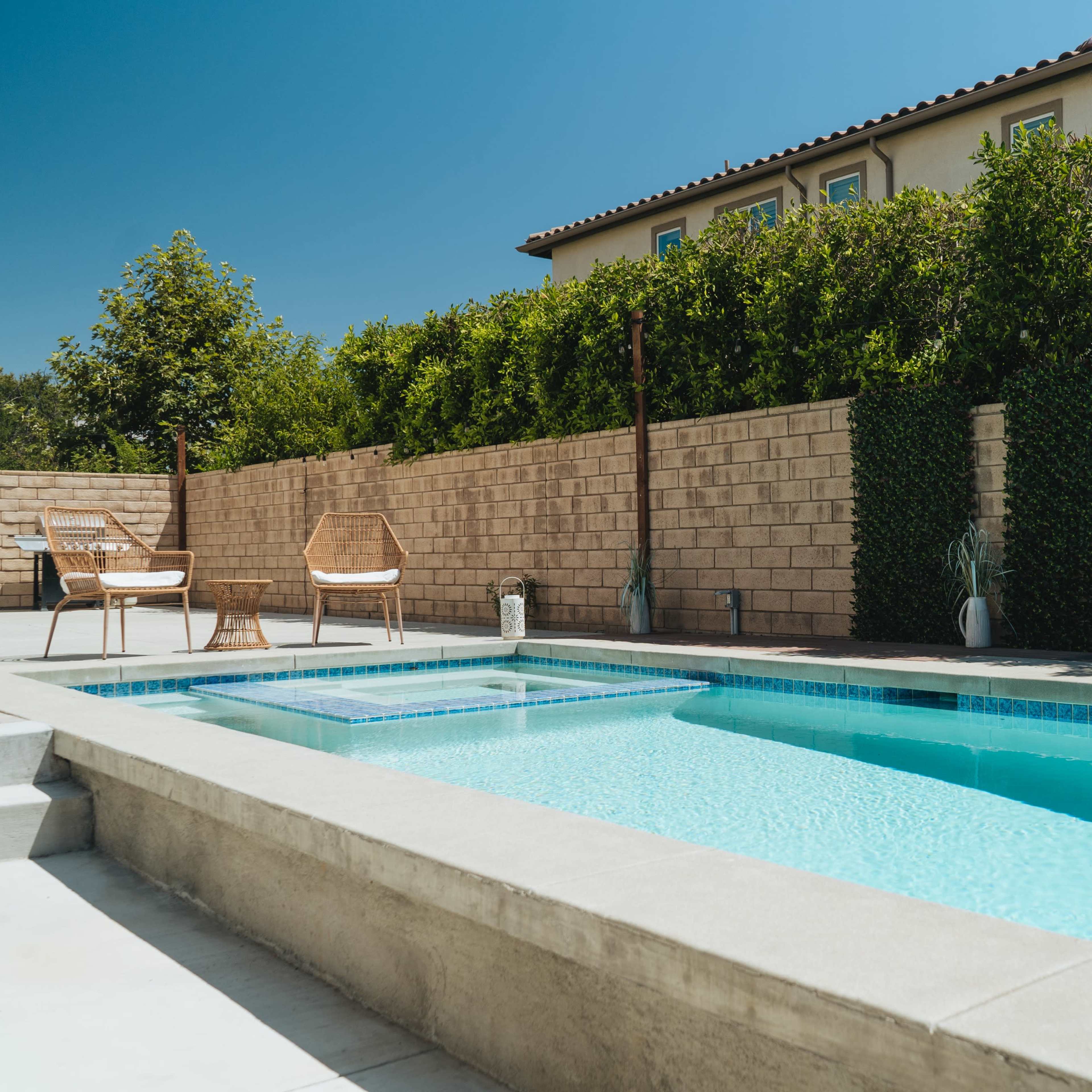 A clear swimming pool beside a patio area with two chairs and a well-maintained garden wall in the background.