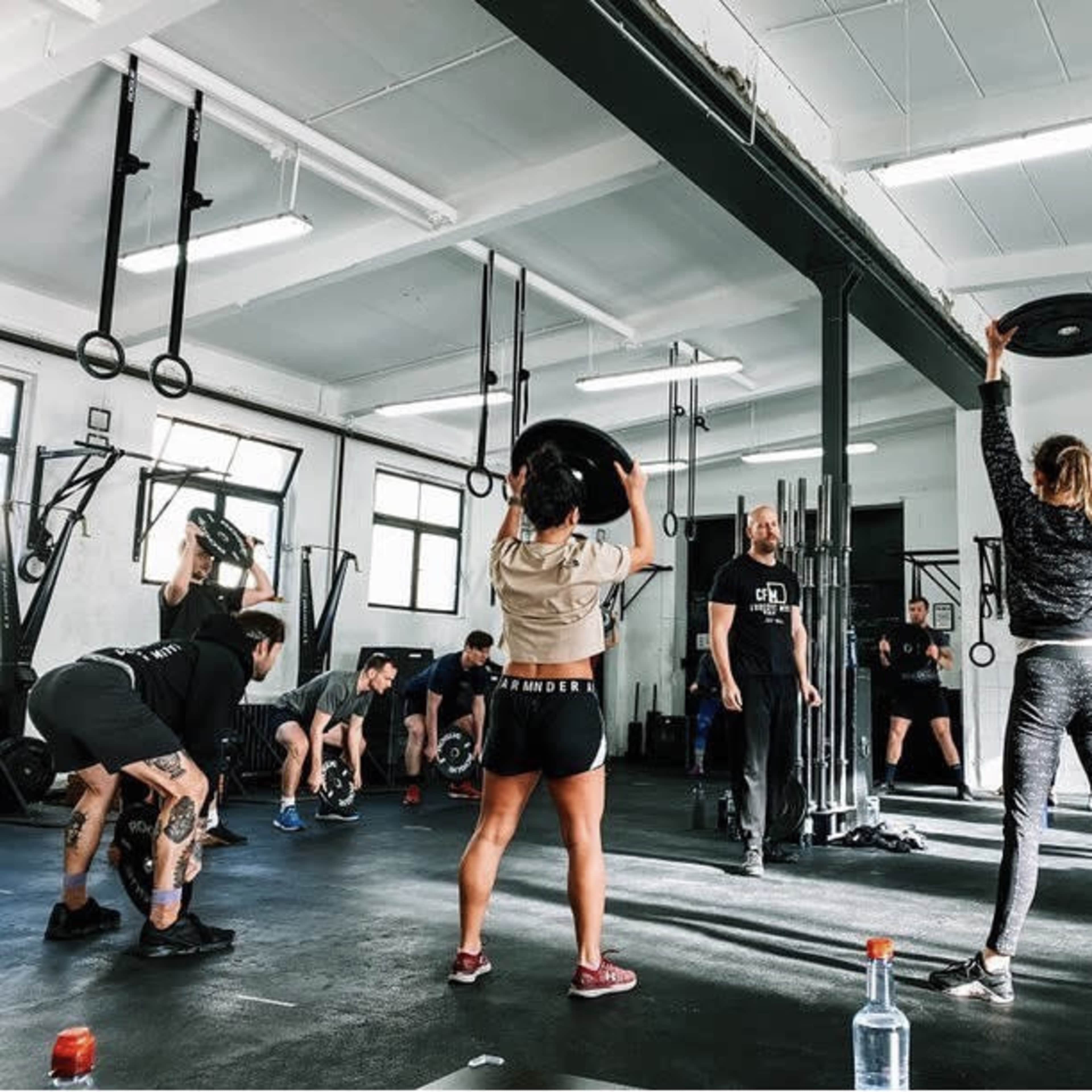 A group of people is engaged in a fitness class, lifting weights and following instructions in a well-equipped gym.