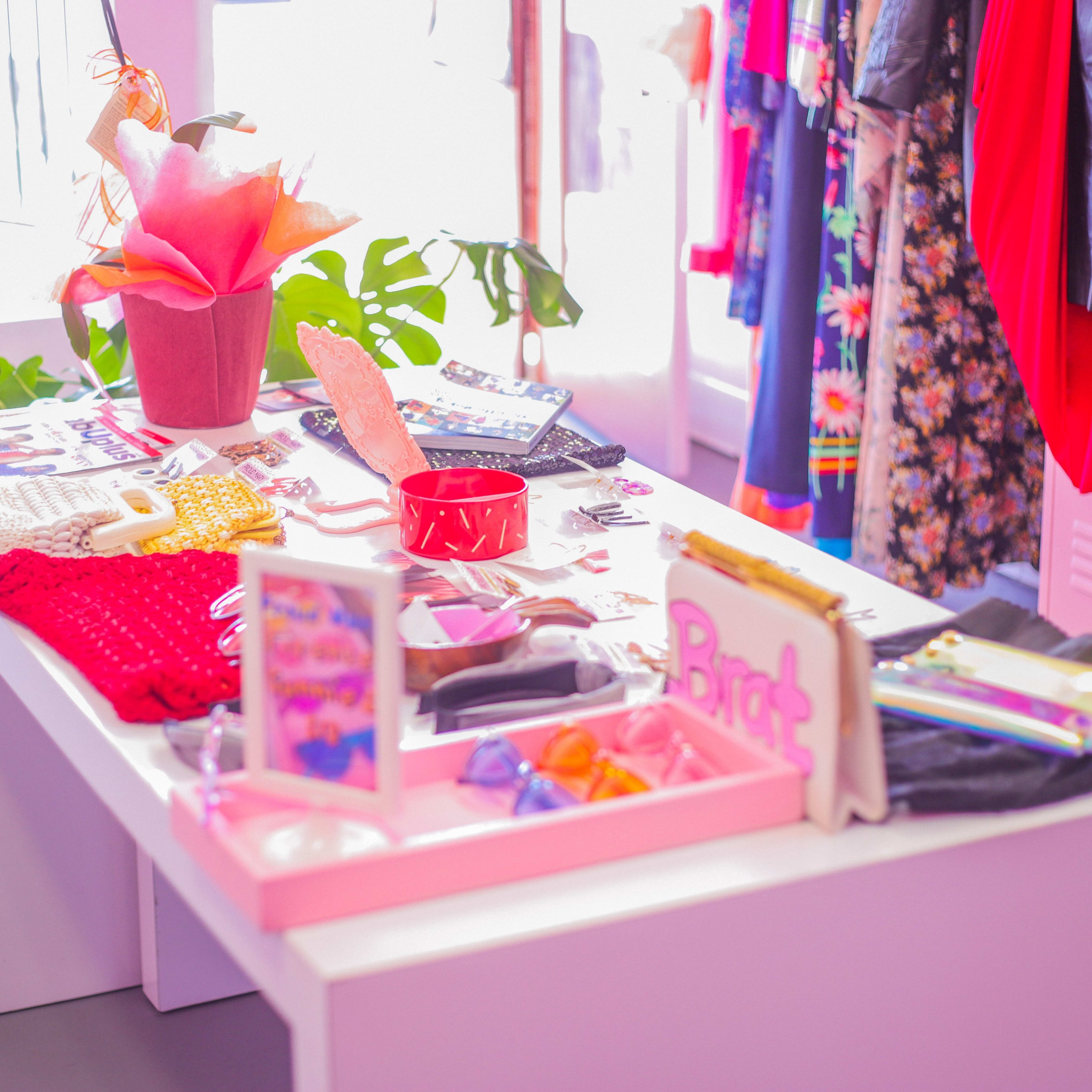 A display table with various accessories and clothing items is set in a brightly lit shop surrounded by hanging garments.