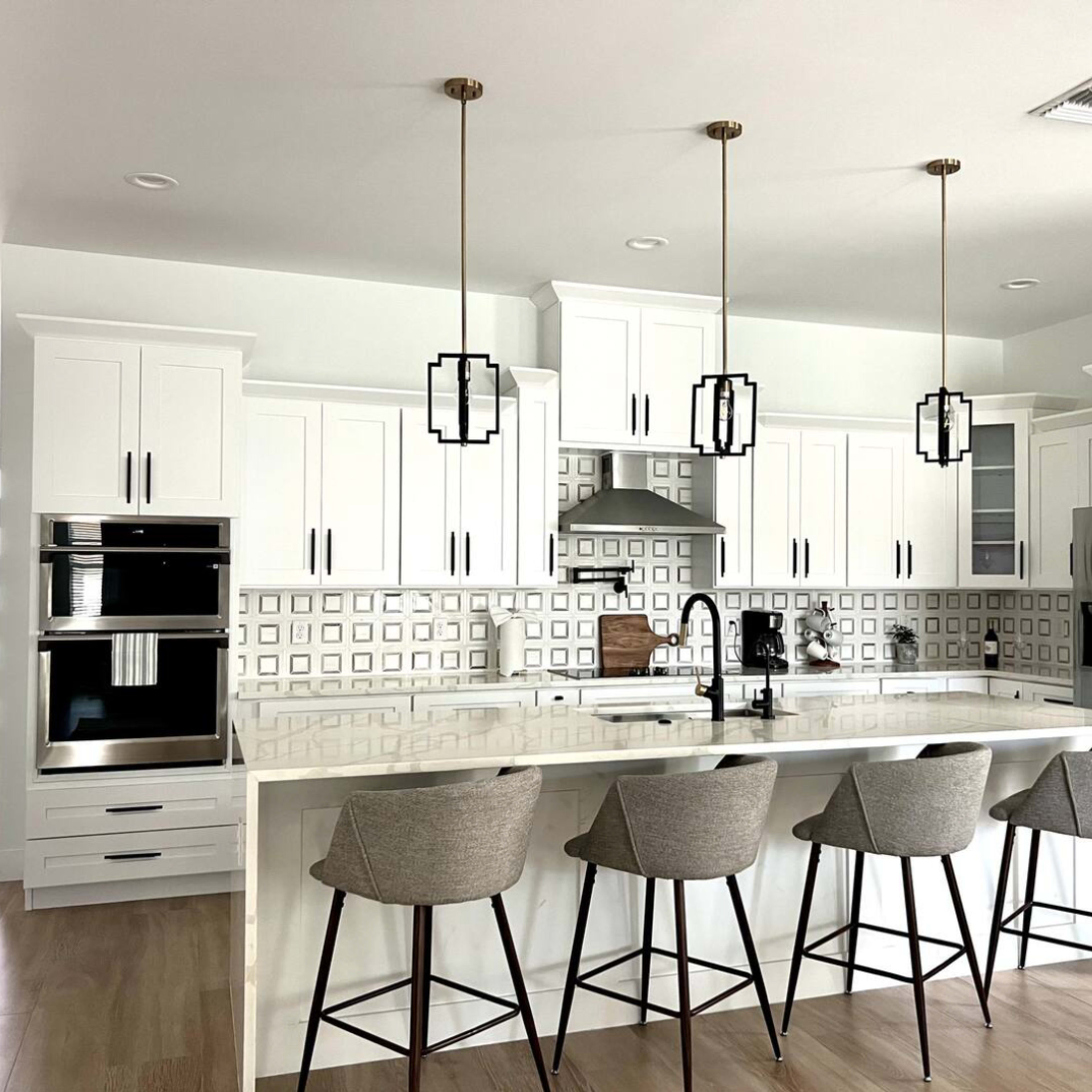 A modern kitchen with white cabinetry, a large island with four bar stools, and three pendant lights hanging above the island.