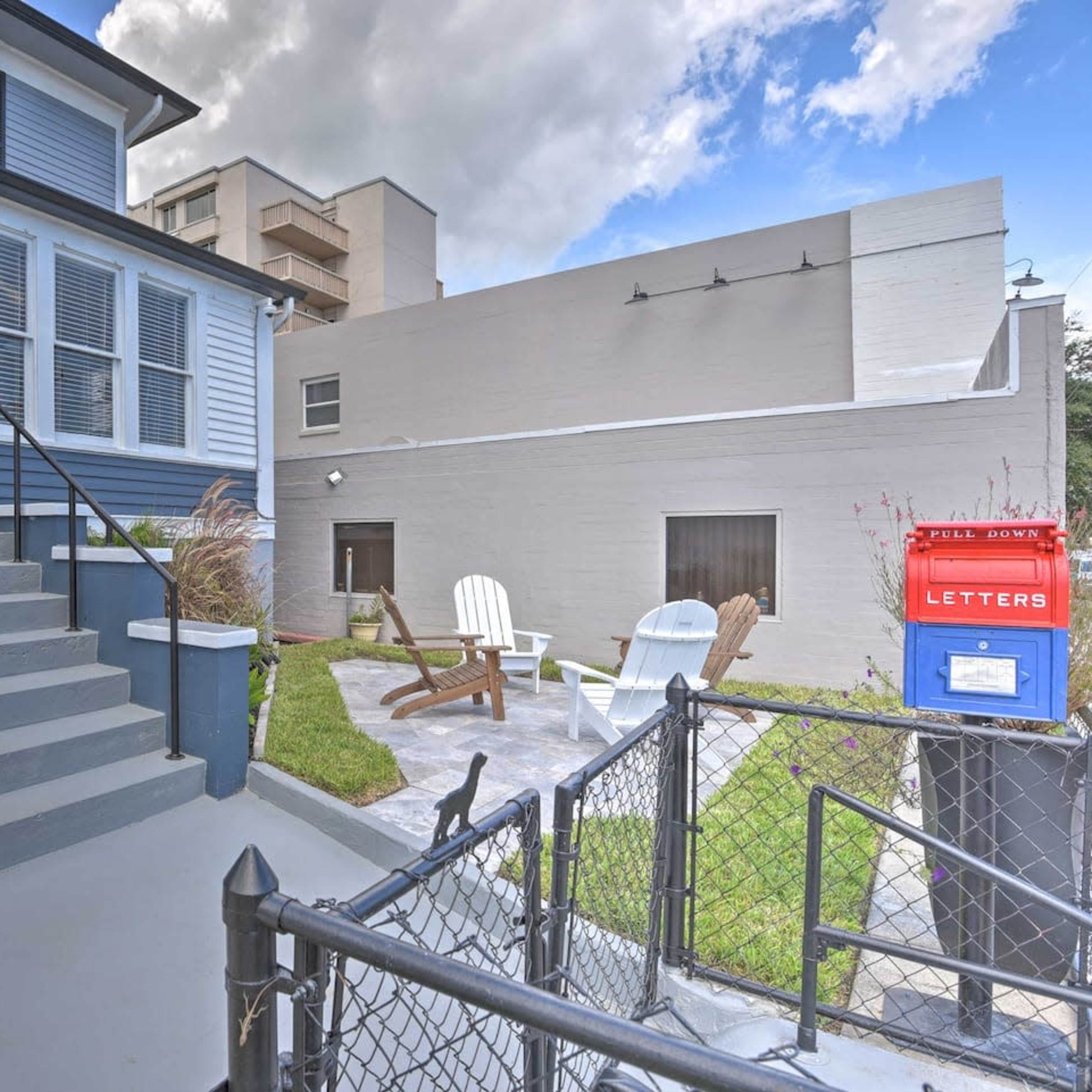 A blue and gray house features a front entrance with stairs and a fence, alongside a red mailbox and a small outdoor seating area.