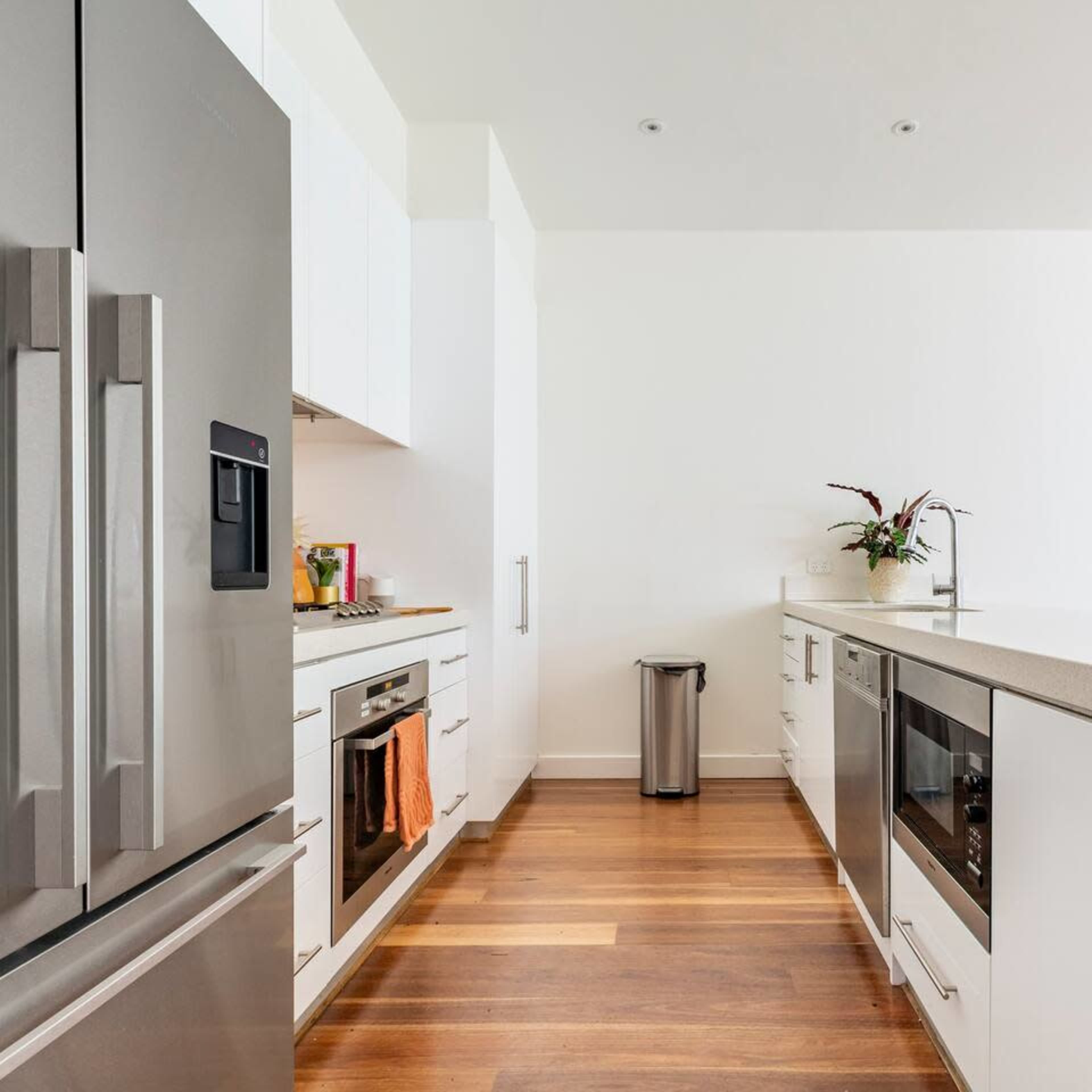 A modern kitchen features stainless steel appliances, wooden flooring, and white cabinetry.