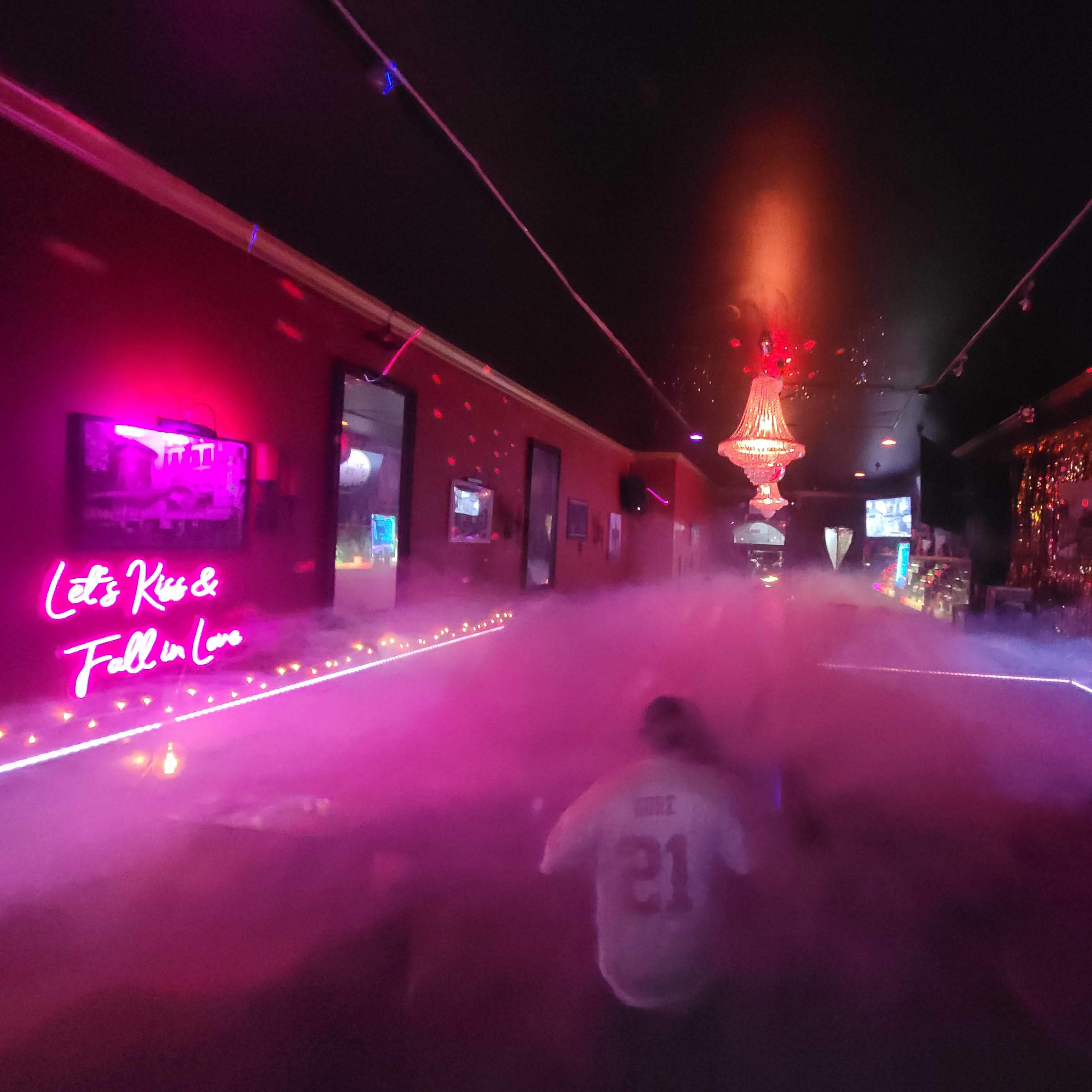 A dimly lit room with colorful neon signs, a chandelier, and a foggy atmosphere.