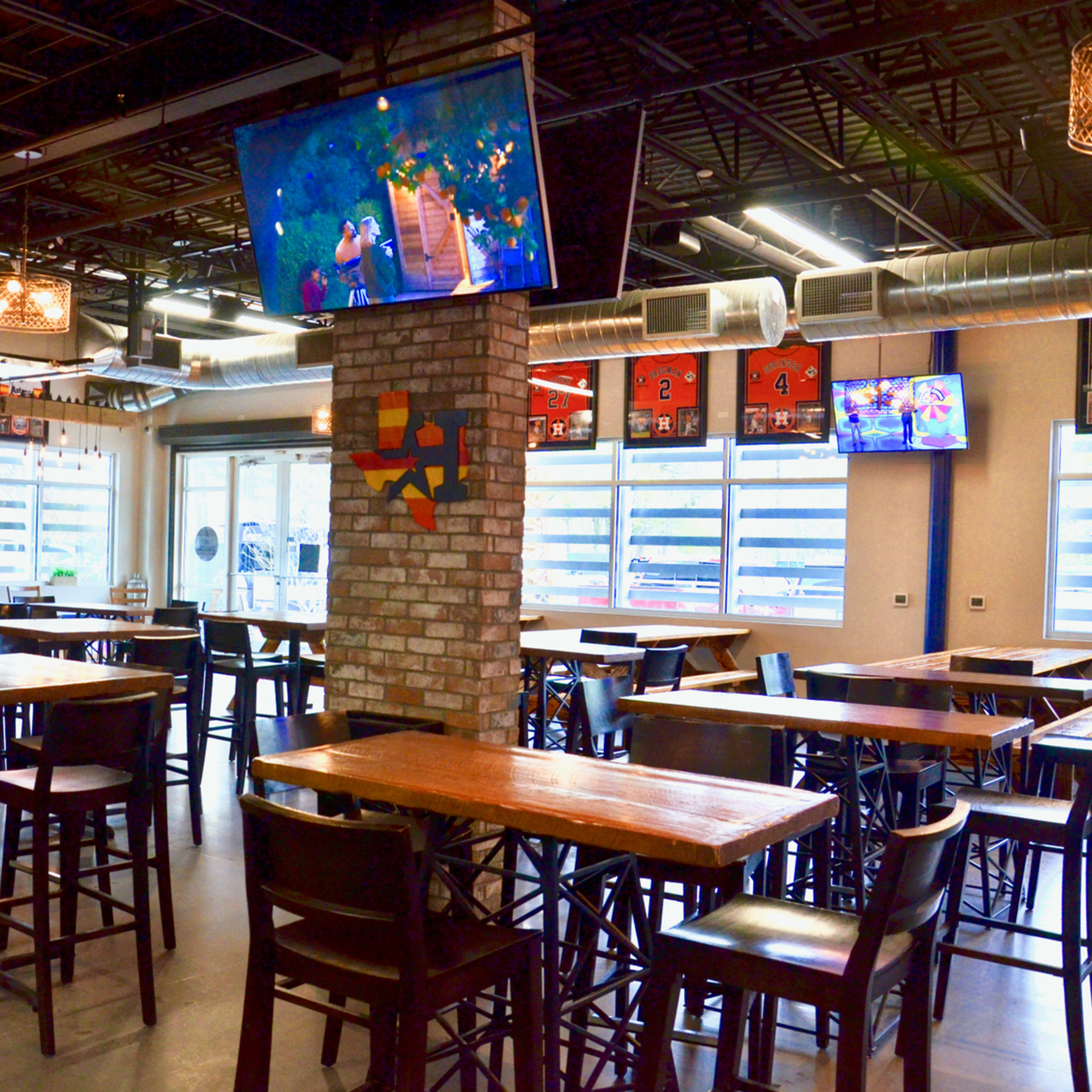A spacious dining area with wooden tables and chairs, large windows, and multiple televisions mounted on the walls.