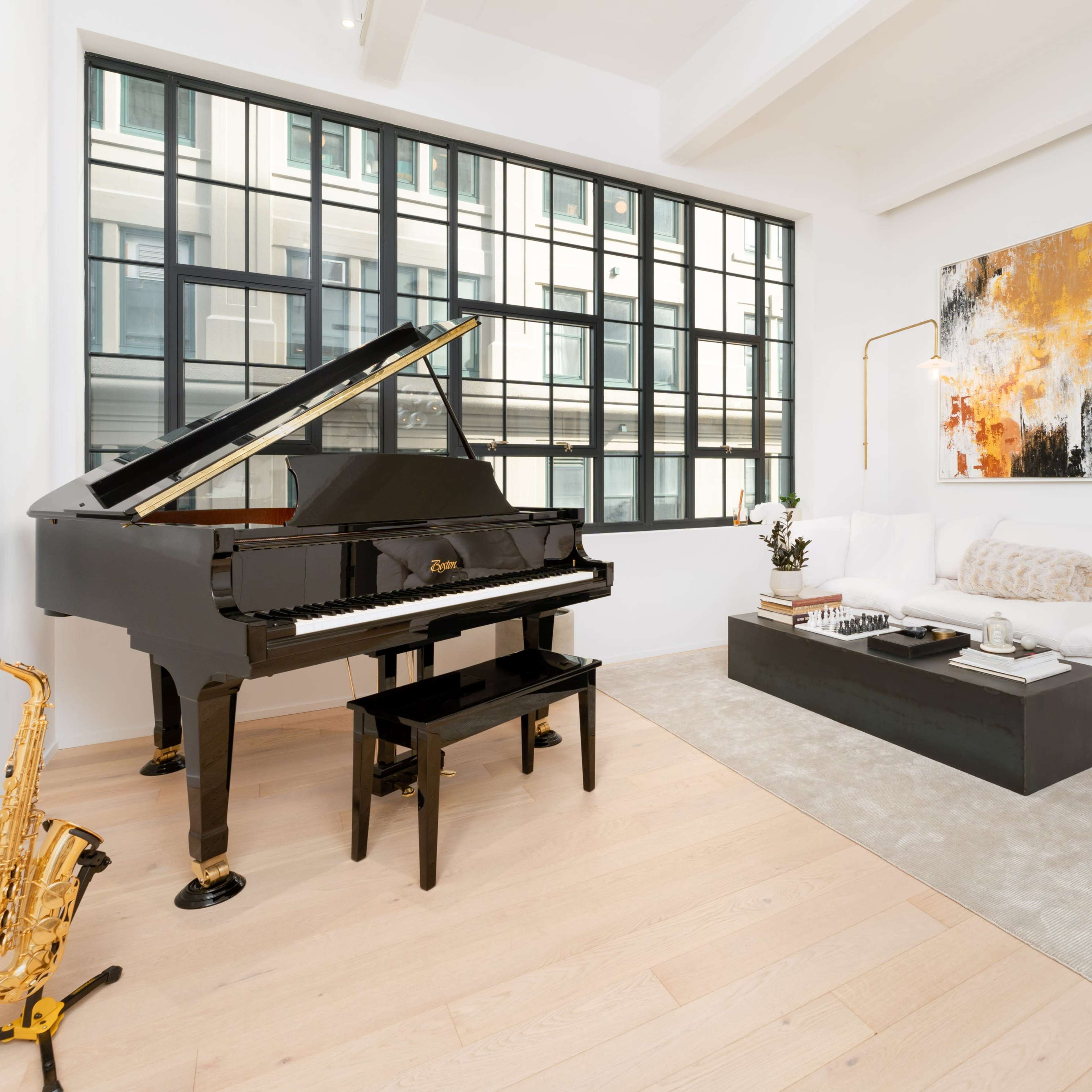 A black piano and a saxophone are positioned beside a white sofa and coffee table in a bright, minimalist living room with large windows.