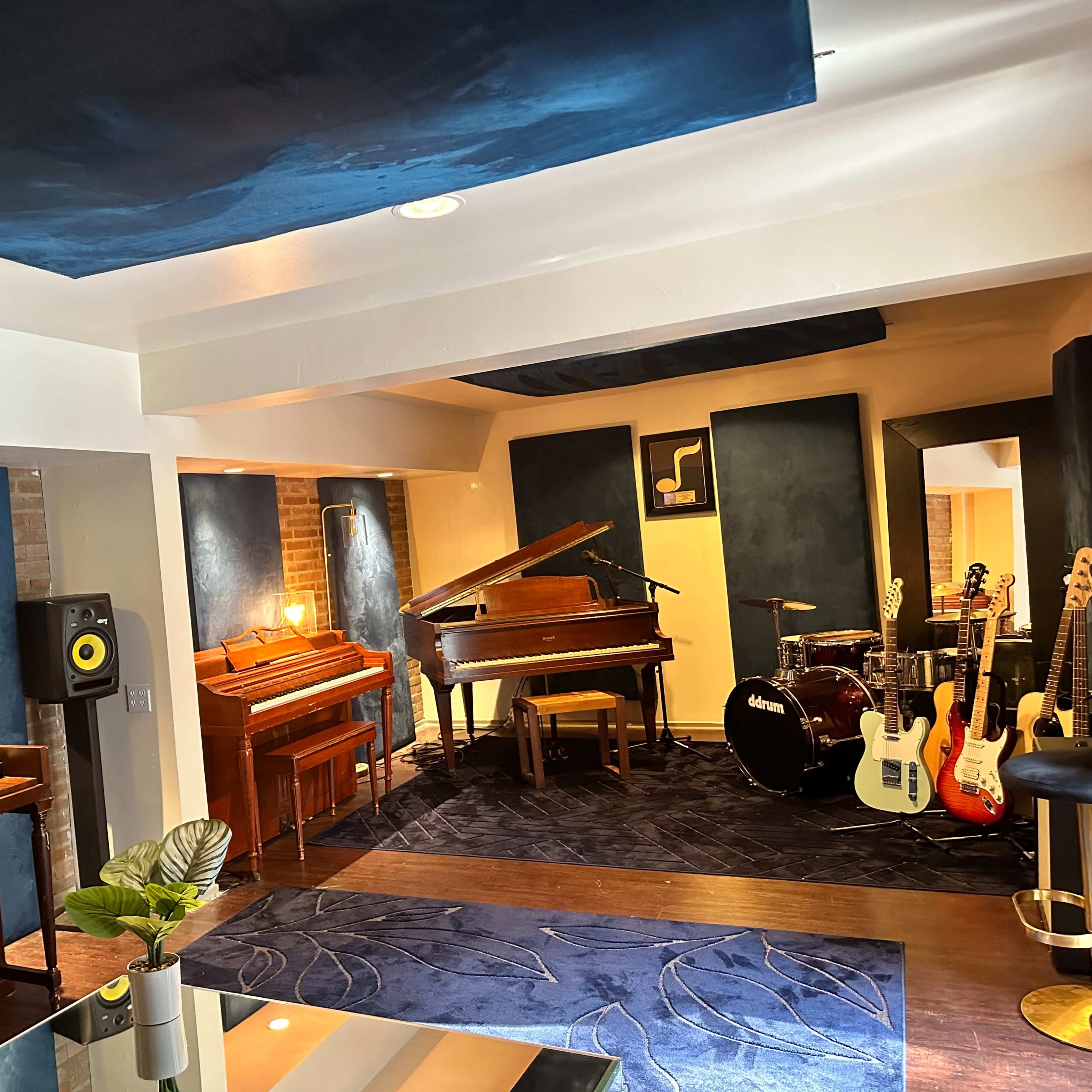 A music studio featuring a grand piano, an upright piano, various musical instruments, and soundproofed walls in a well-lit room.