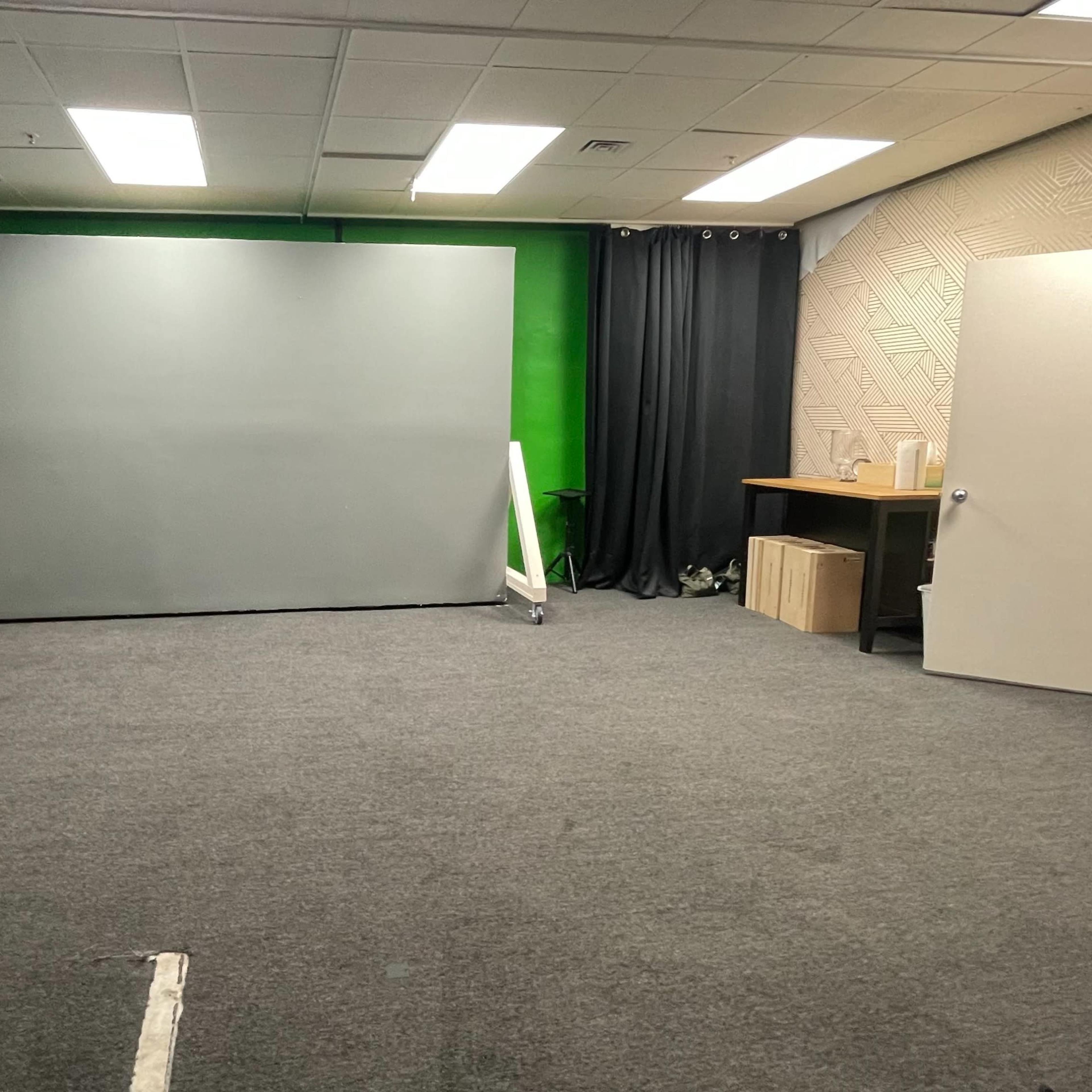An empty studio space with a gray backdrop, green wall, and various furnishings including a shelving unit and a table.