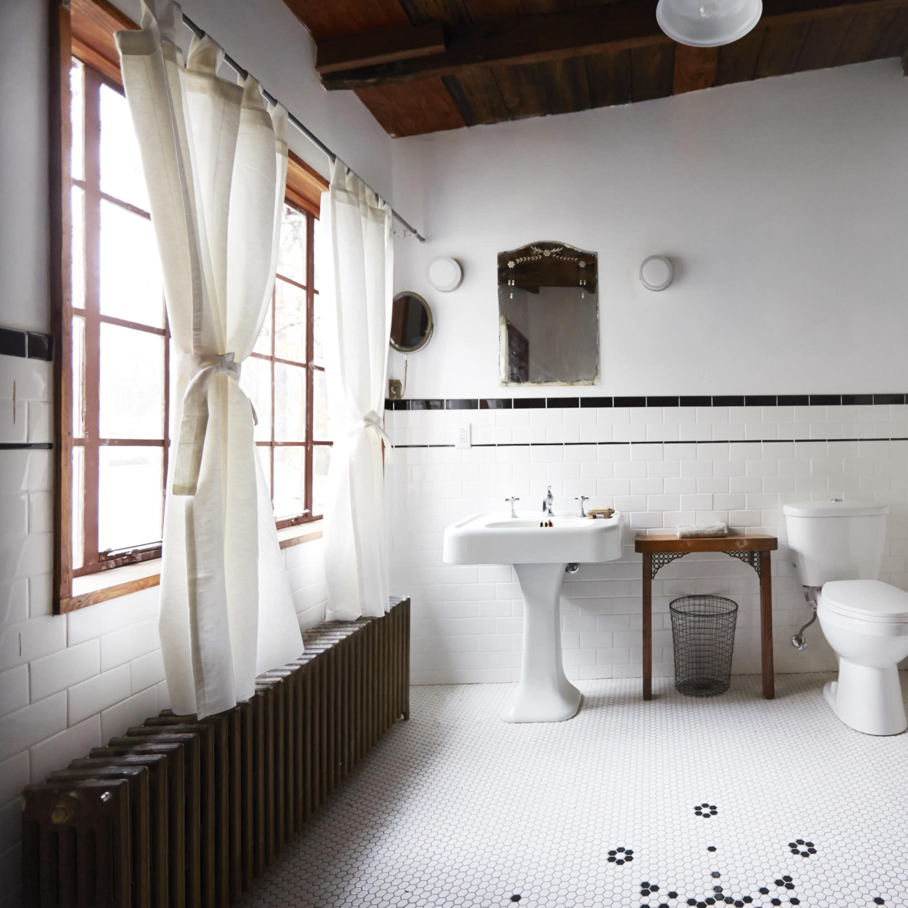 A bathroom with a white tiled floor, a pedestal sink, a toilet, and a large window allowing natural light to enter.