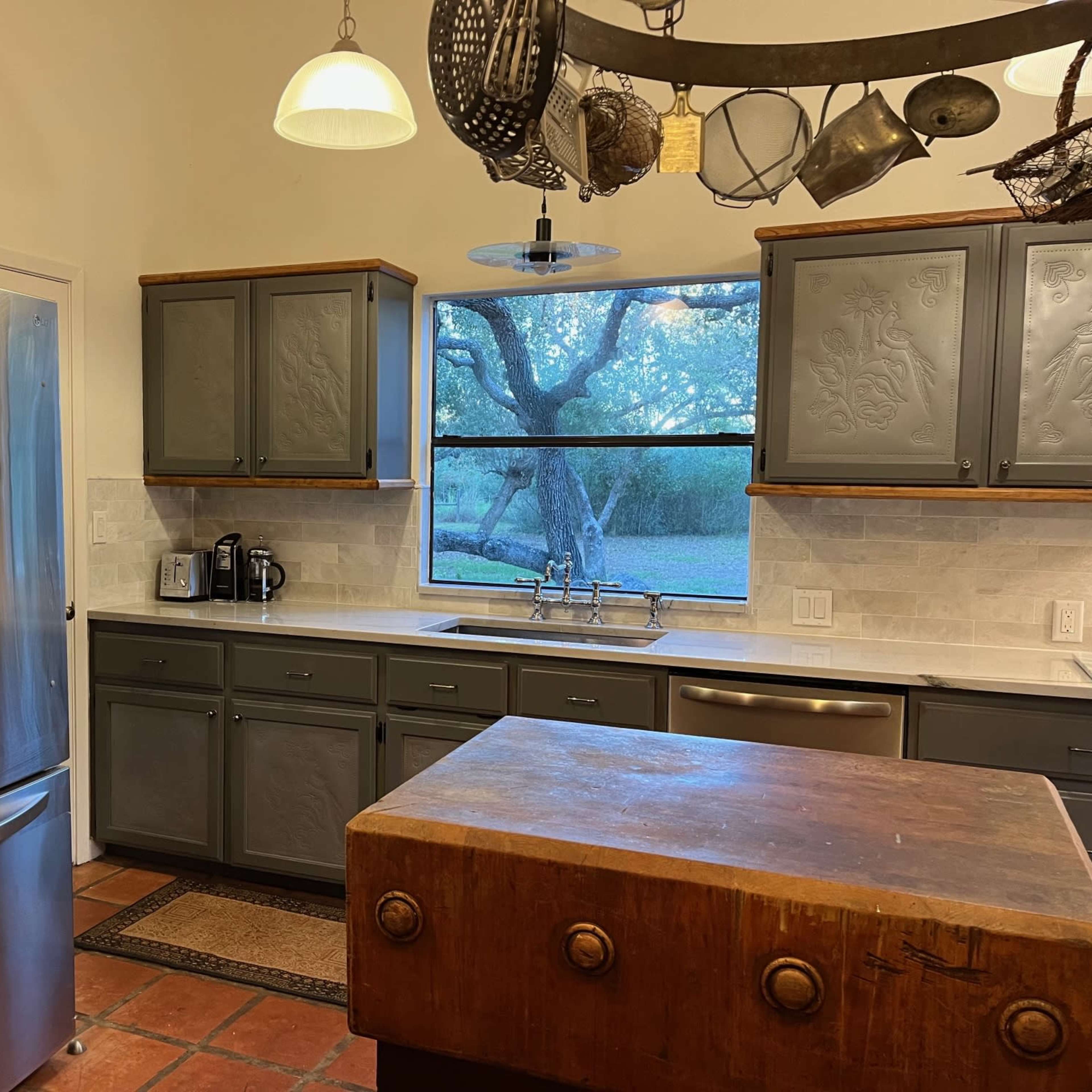 A kitchen features stainless steel appliances, gray cabinets, and a wooden island, with a window overlooking an outdoor tree.