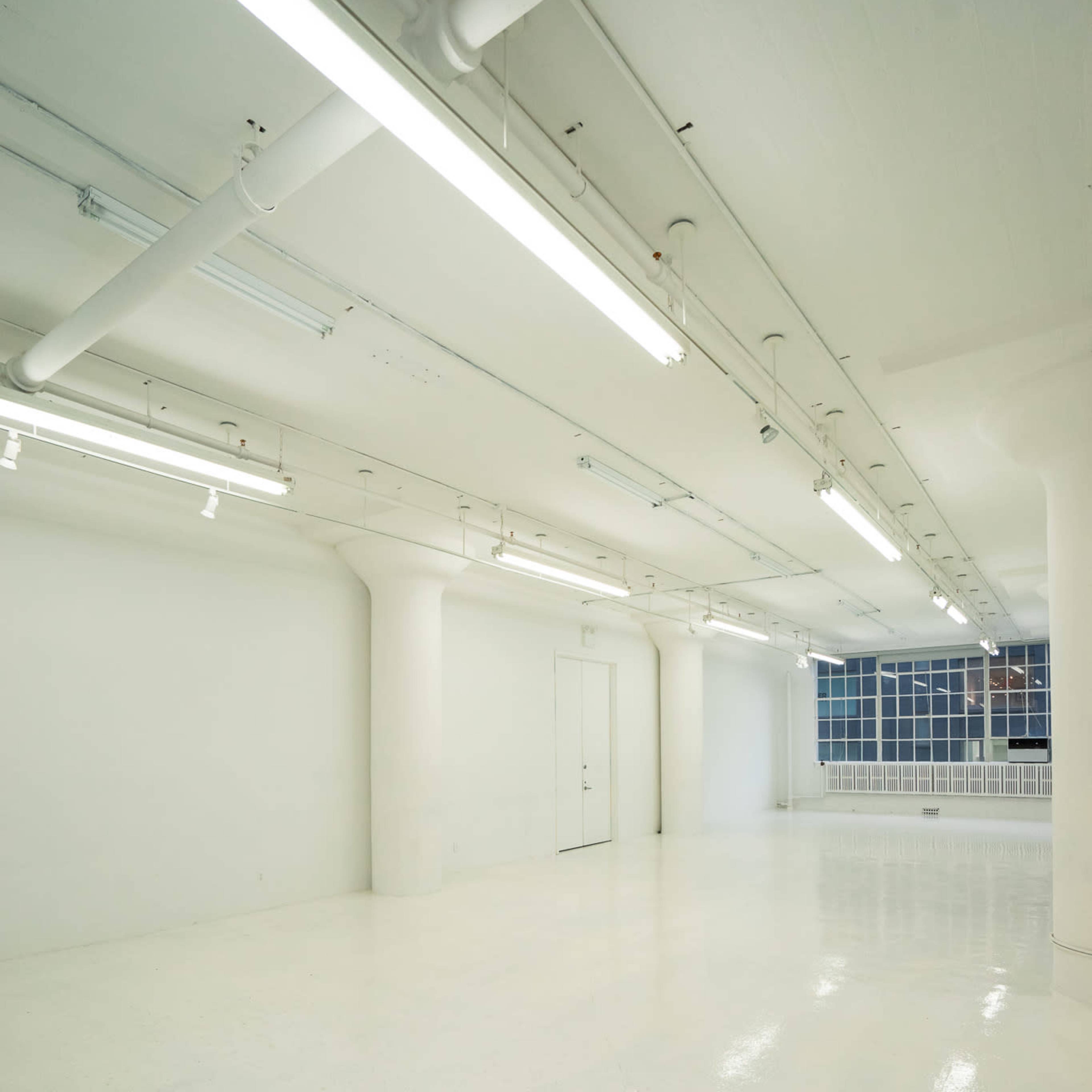 A spacious, empty white room with fluorescent lighting and large windows.