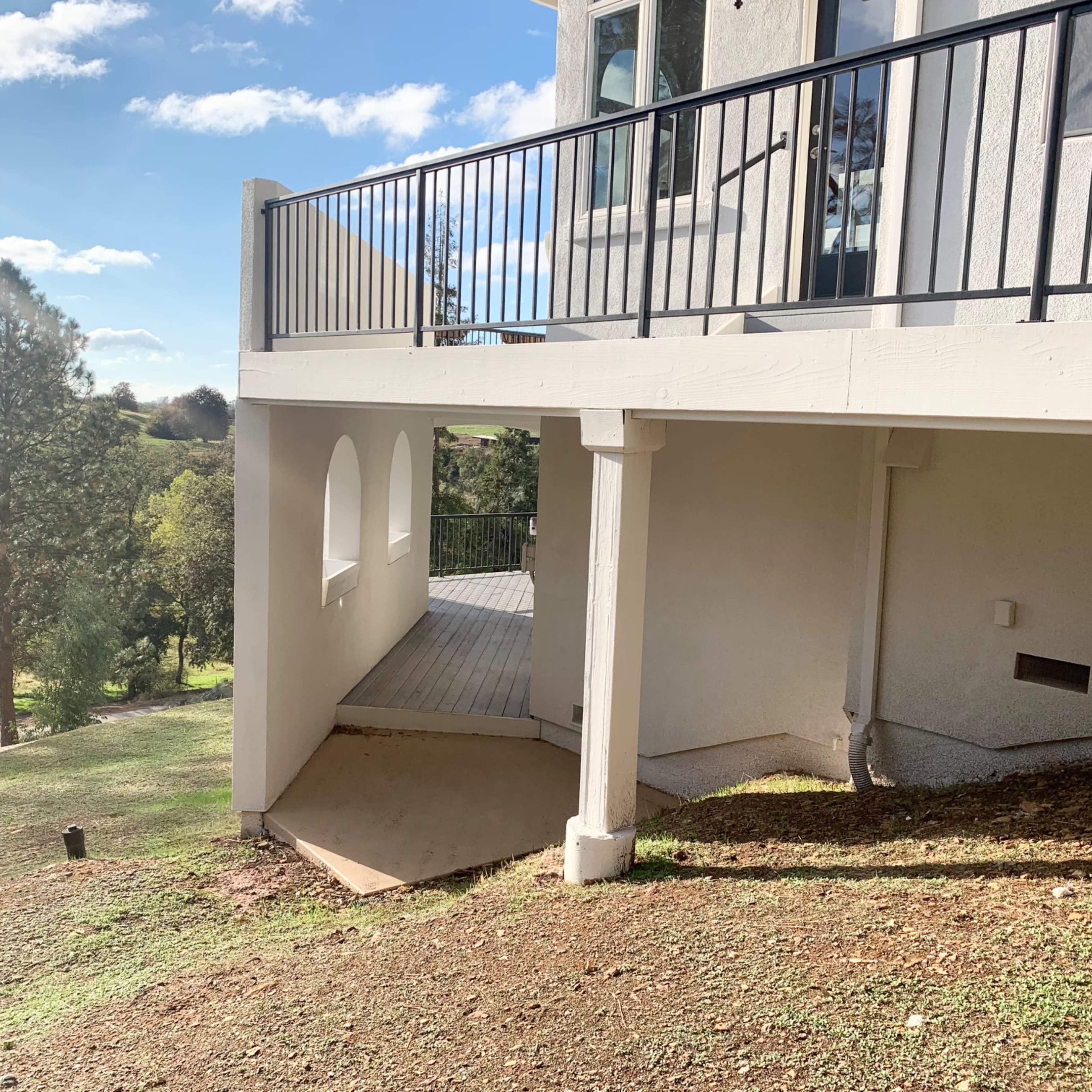 A two-level building with a balcony overlooking a grassy area and trees, under a clear blue sky.