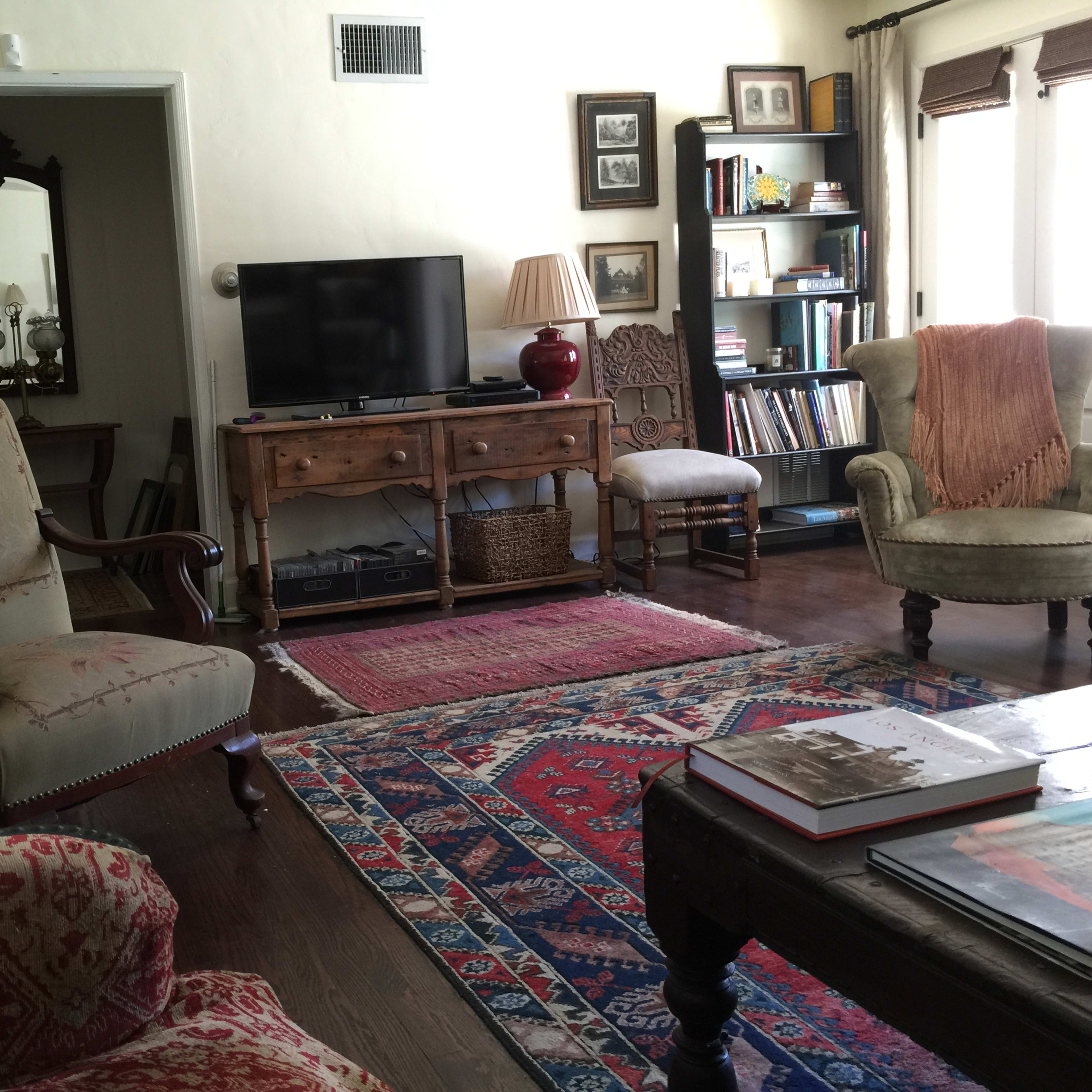 A living room with a mix of seating, a television on a wooden console, bookshelves, and a patterned rug.