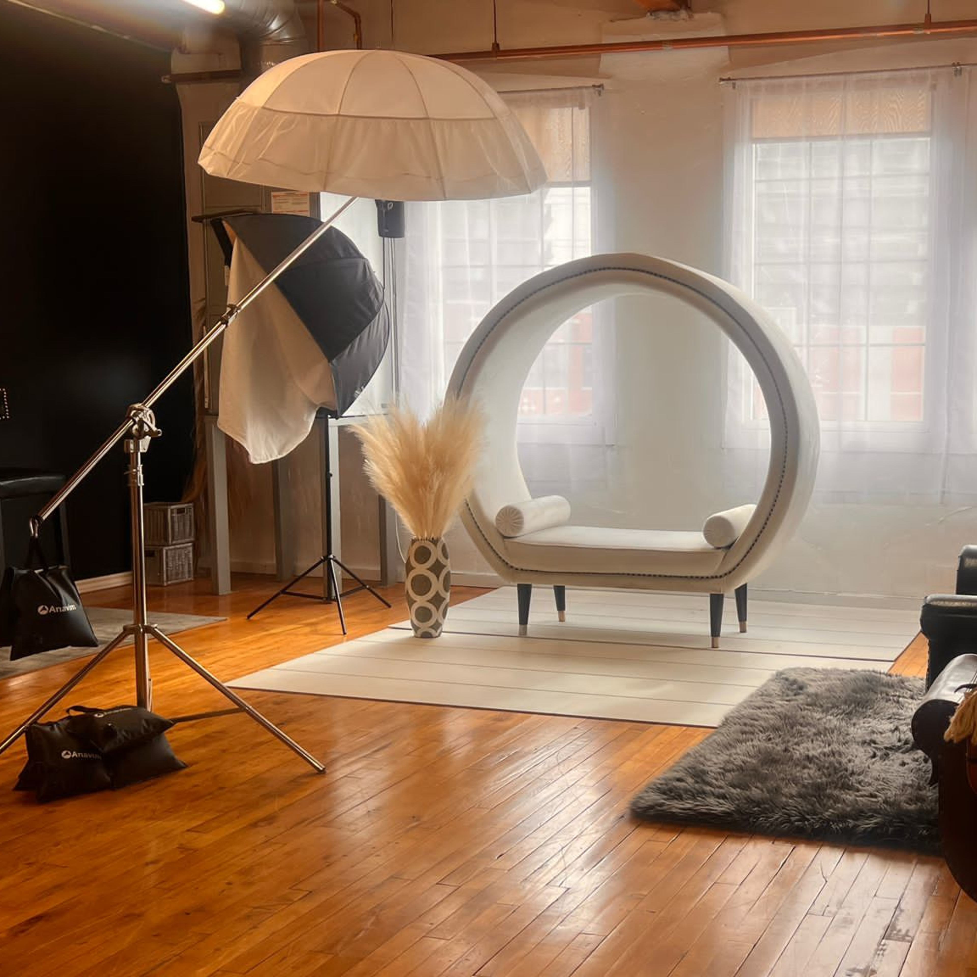 A stylish photo studio interior featuring a modern circular chair, soft lighting equipment, and a variety of seating arrangements on wooden flooring.