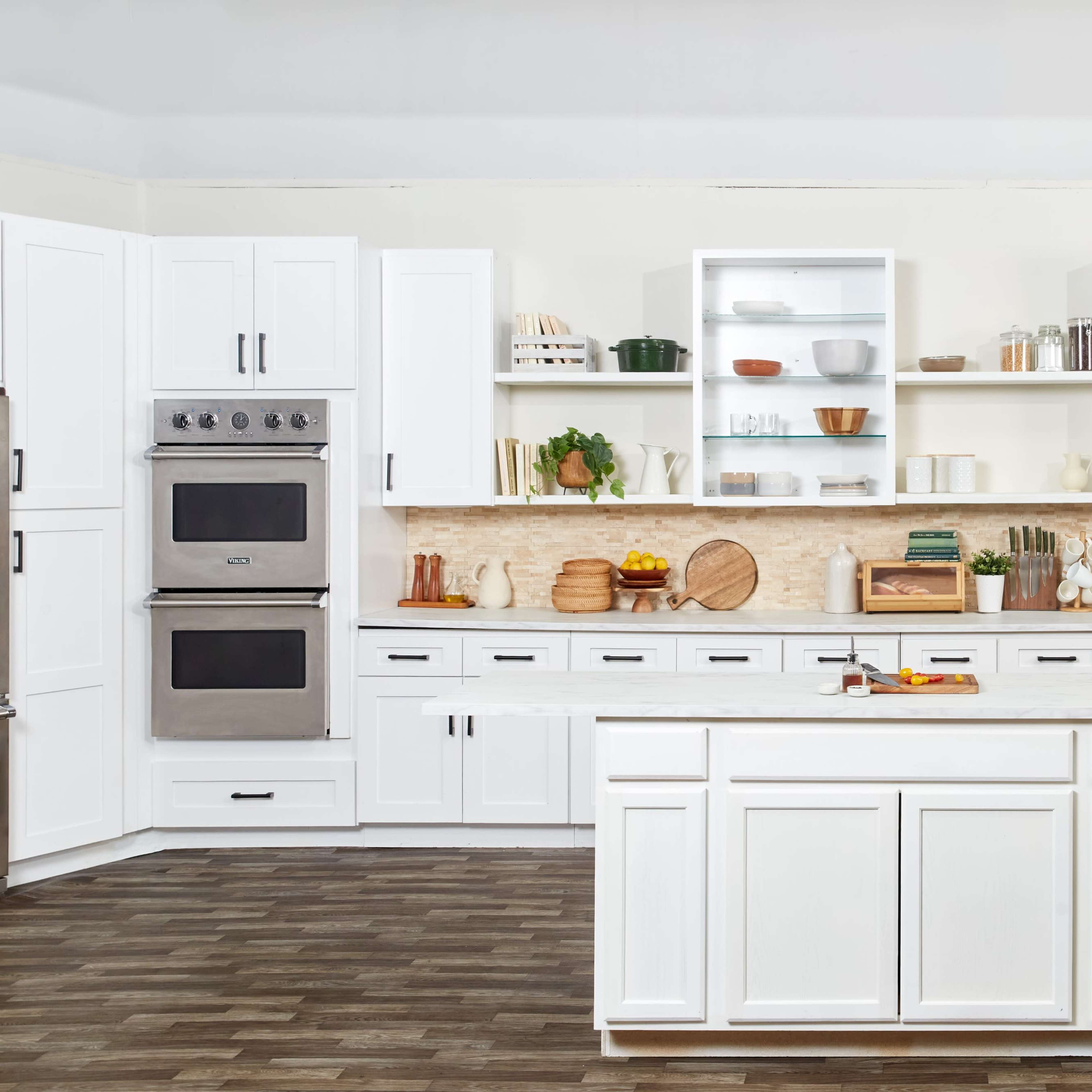 A modern kitchen features white cabinetry, a central island, and open shelves displaying various dishes and wooden kitchenware.