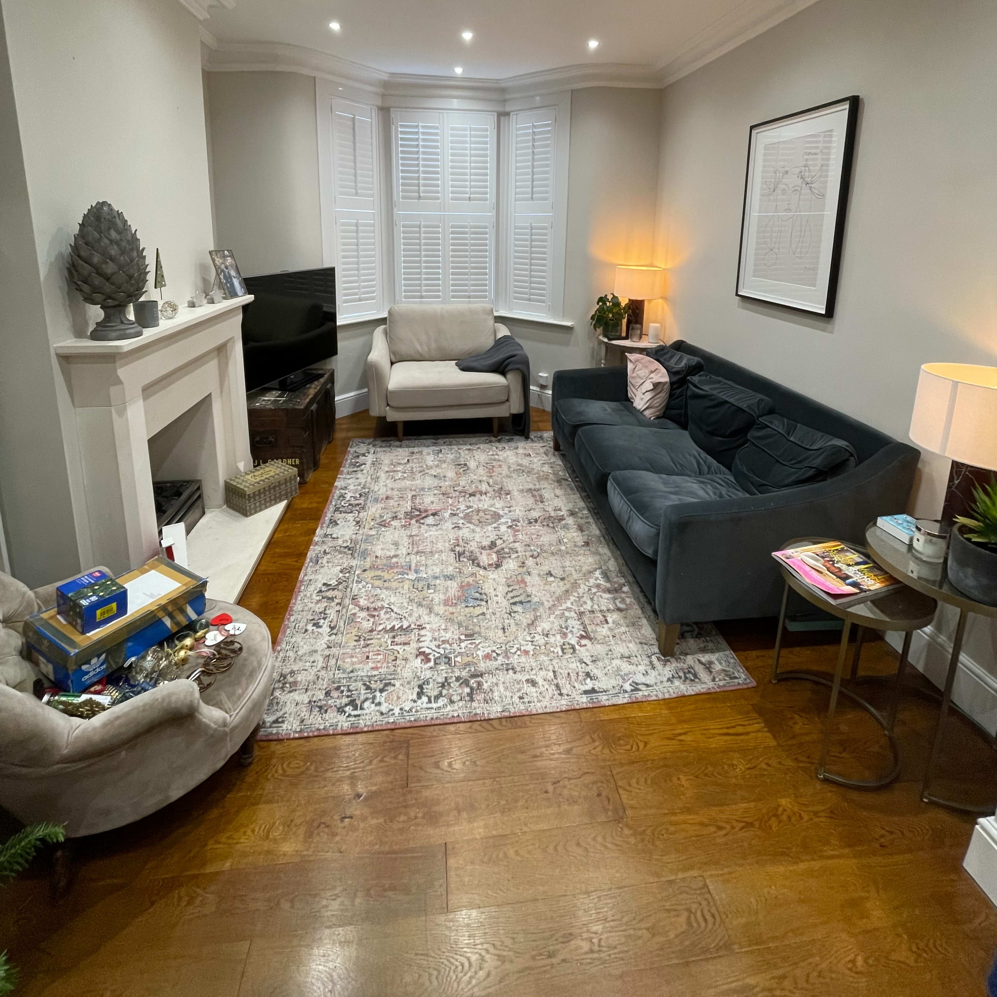 A living room features two sofas, a television, a fireplace, and a patterned rug on wooden flooring.